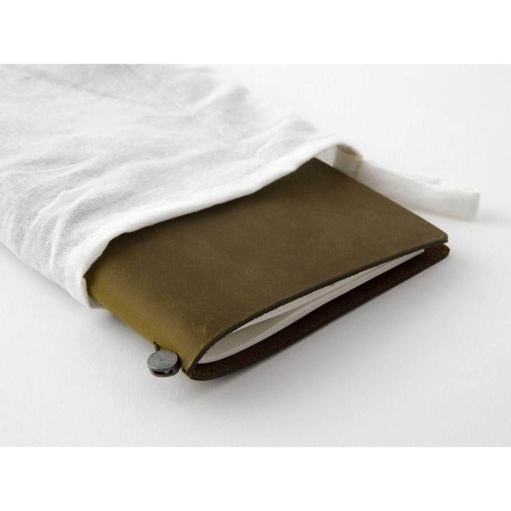 A brown leather-bound notebook with a white cloth bag partially covering it, resting on a white surface.