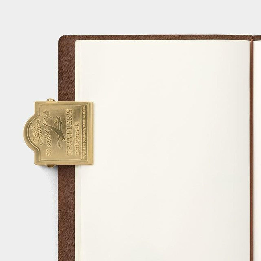 a gold-colored metal clip or bookmark attached to the edge of a blank notebook or page.