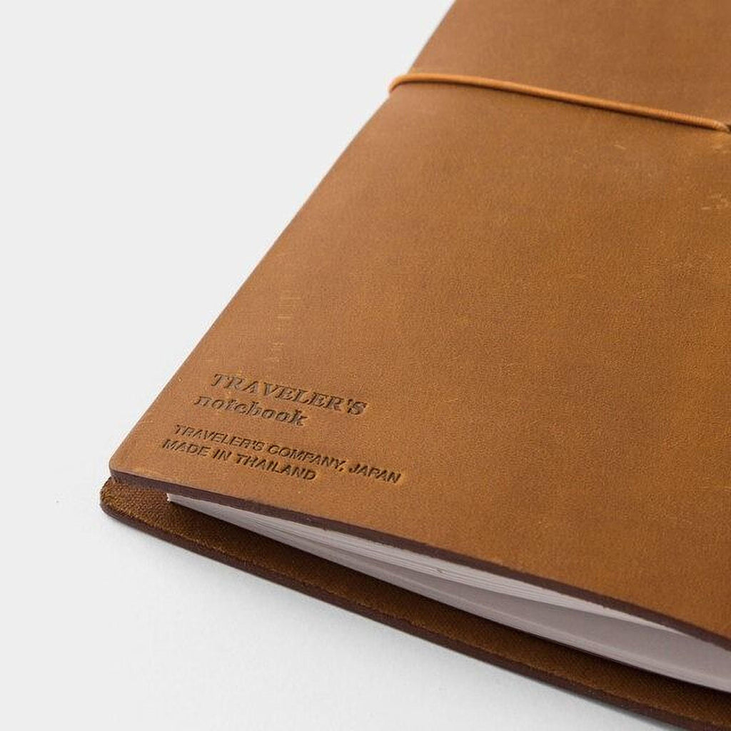 A brown leather-bound notebook with the text "TRAVELER'S NOTEBOOK" printed on the cover.
