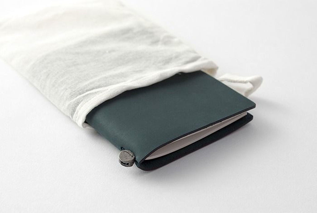 A dark green notebook or journal is partially covered by a white cloth, with a metal clip or zipper attached to the cover.