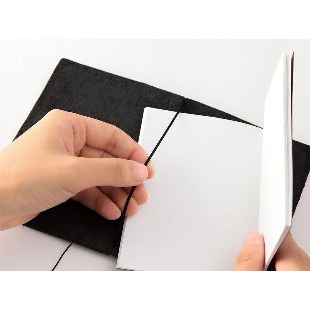 A person's hand is holding open a black notebook with a blank white page inside.