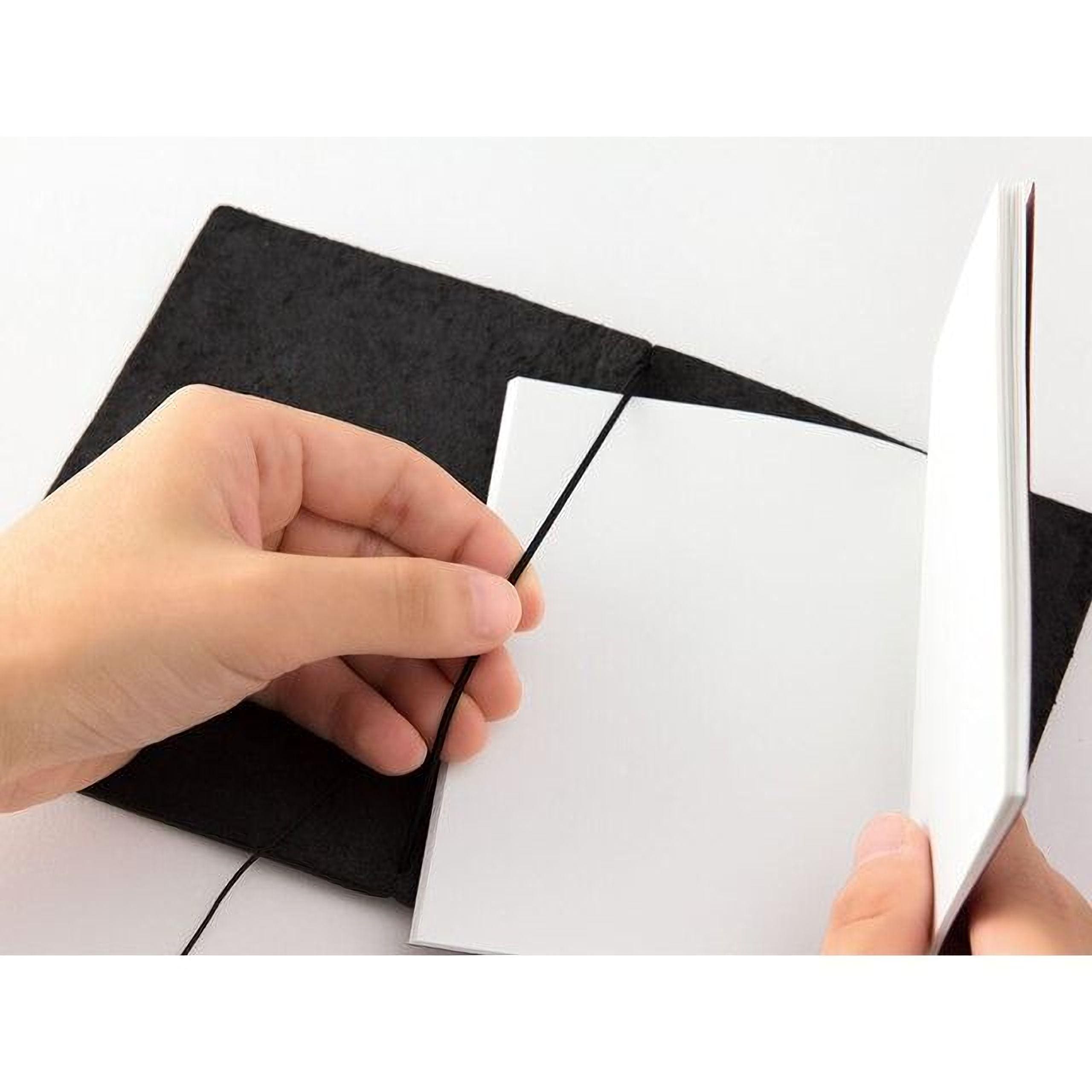 A person's hand is holding open a black notebook with a blank white page inside.