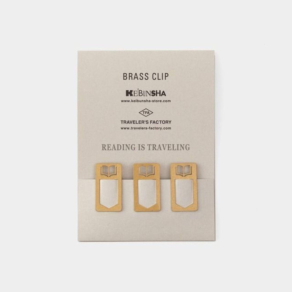 three brass clip holders with book-like designs, arranged on a light-colored background.