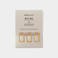 three brass clip holders with book-like designs, arranged on a light-colored background.