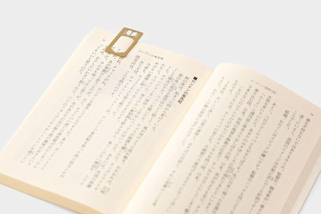 an open book with Japanese text on the pages, and a gold bookmark with a rectangular shape protruding from the top of the page.