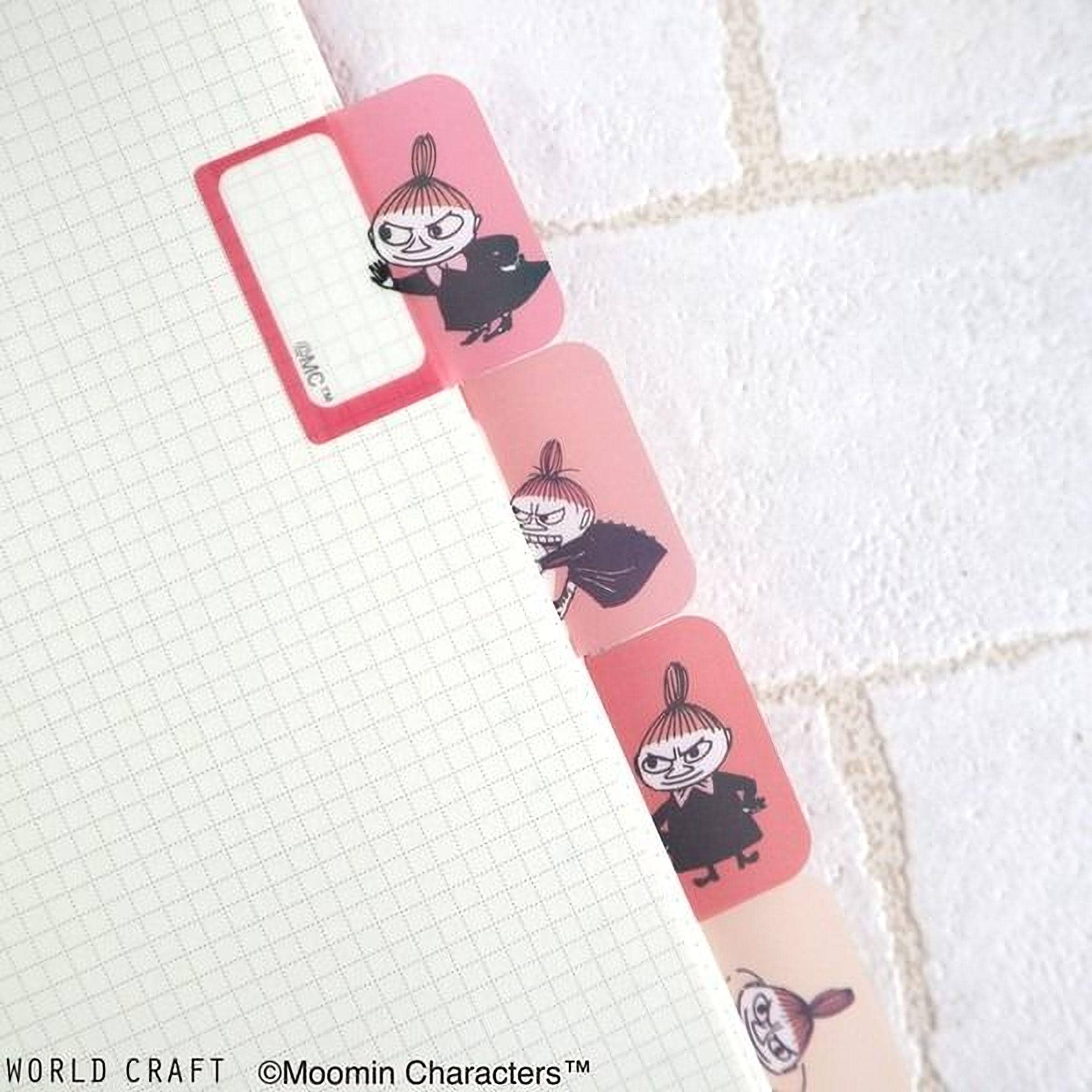 a close-up view of a white notebook with pink dividers, each divider containing a cartoon character. The dividers are arranged in a row, with the first one having a pink frame and the second one having a pink frame with a black character. The image does not contain any text, and the dividers are not described as being part of a larger collage or a series of images.