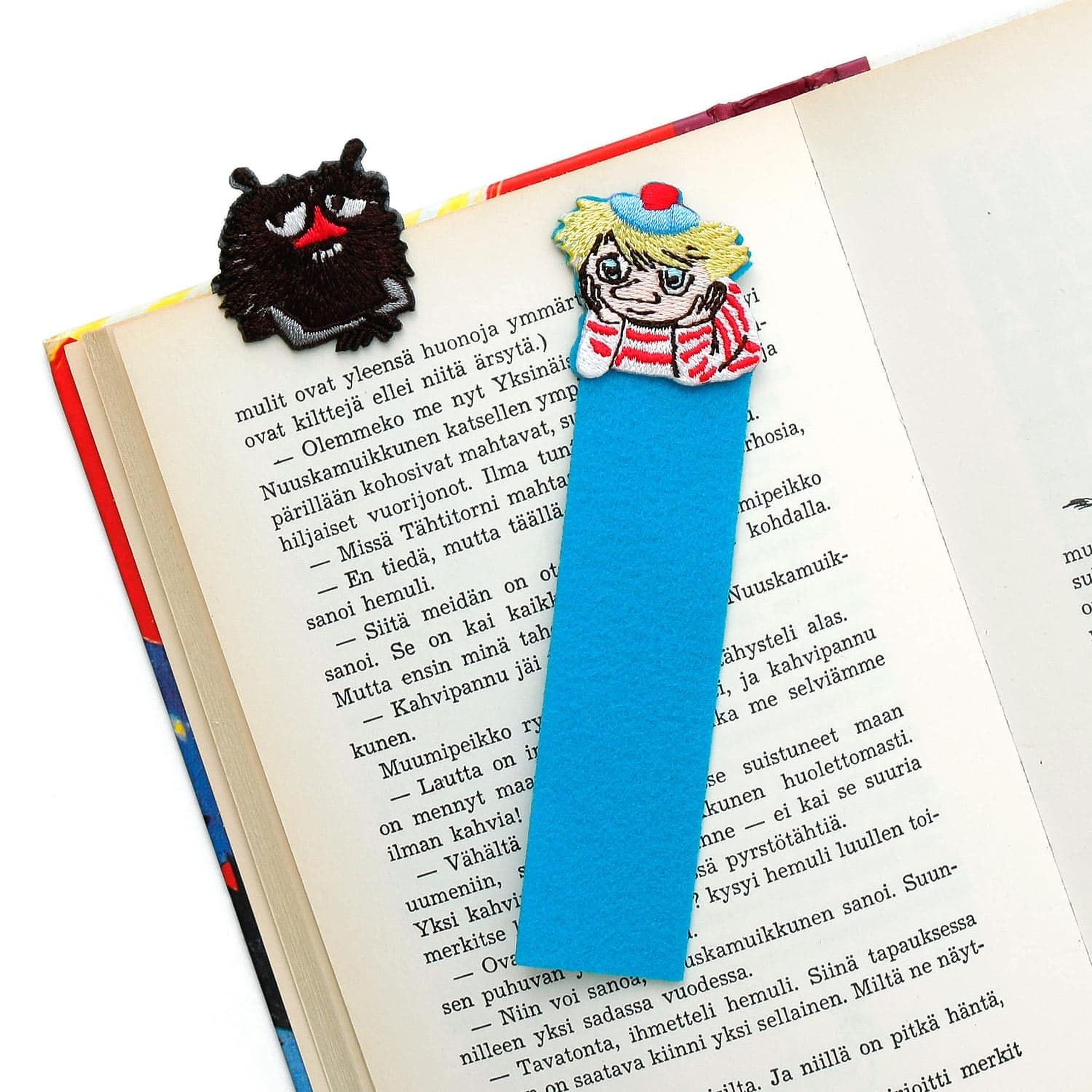 a blue bookmark with a cartoon character on it, placed on top of an open book with text in a foreign language.