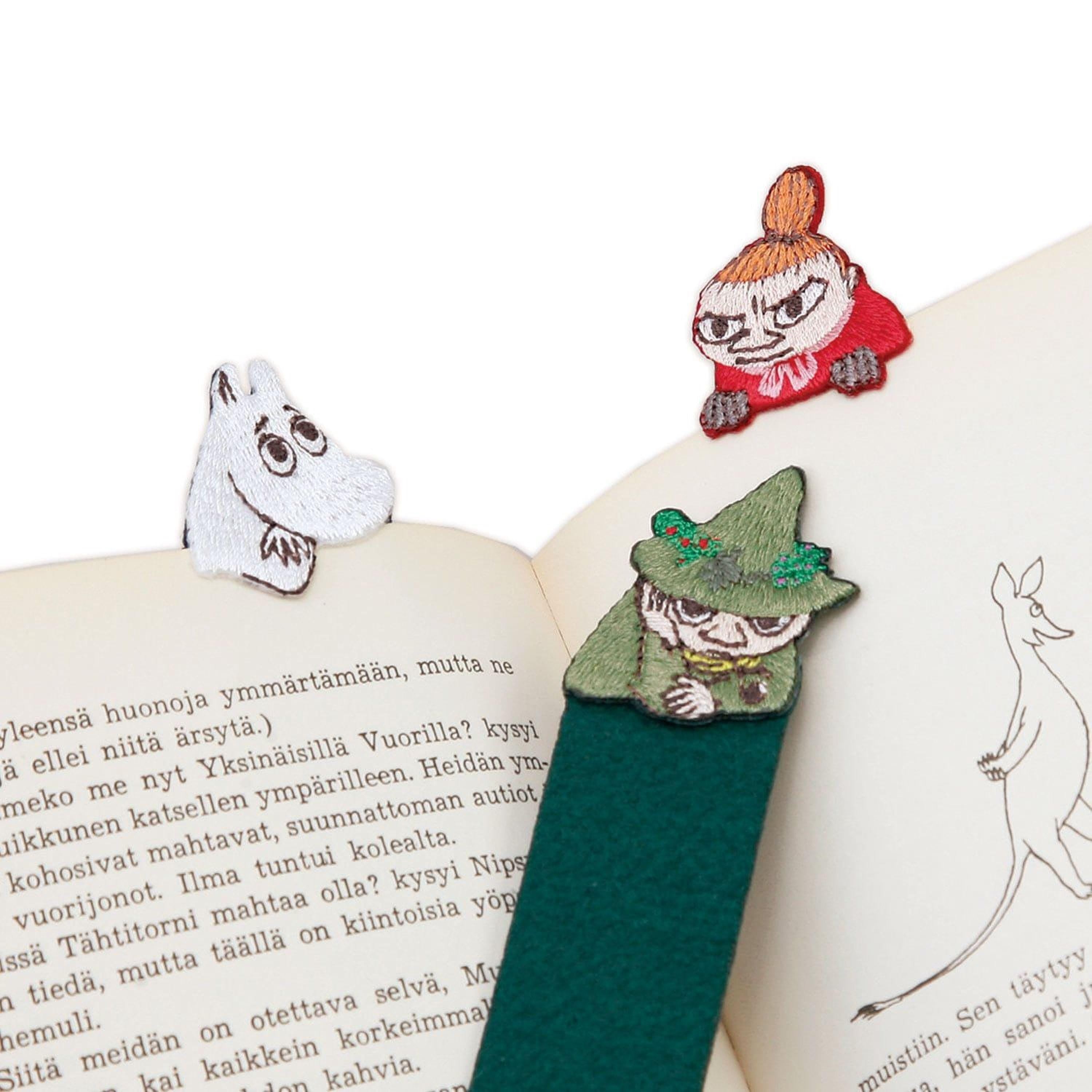 a green bookmark with a whimsical character design, placed on an open book with text visible.