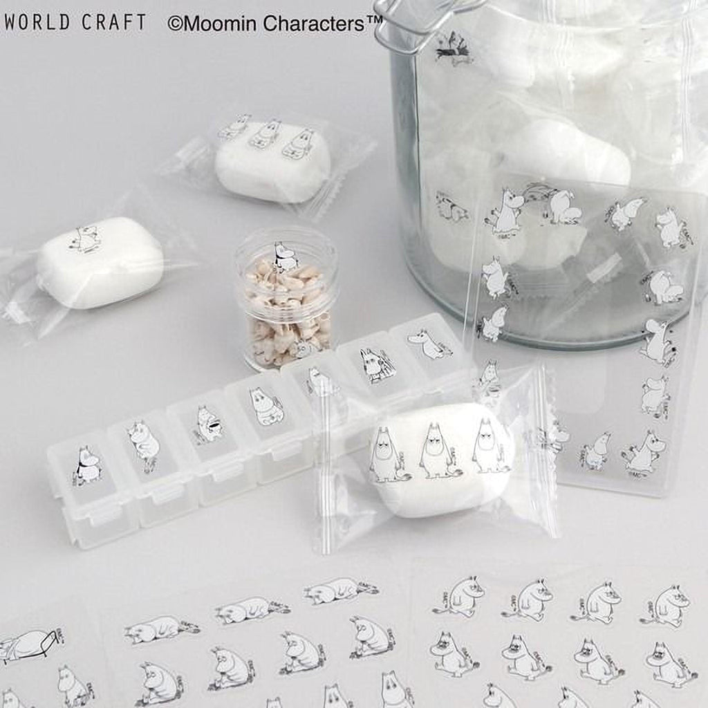 various items related to the Moomin character, including a glass jar filled with white objects, a pill organizer, and several small white objects. The items are arranged on a white surface, with some of them wrapped in clear plastic.