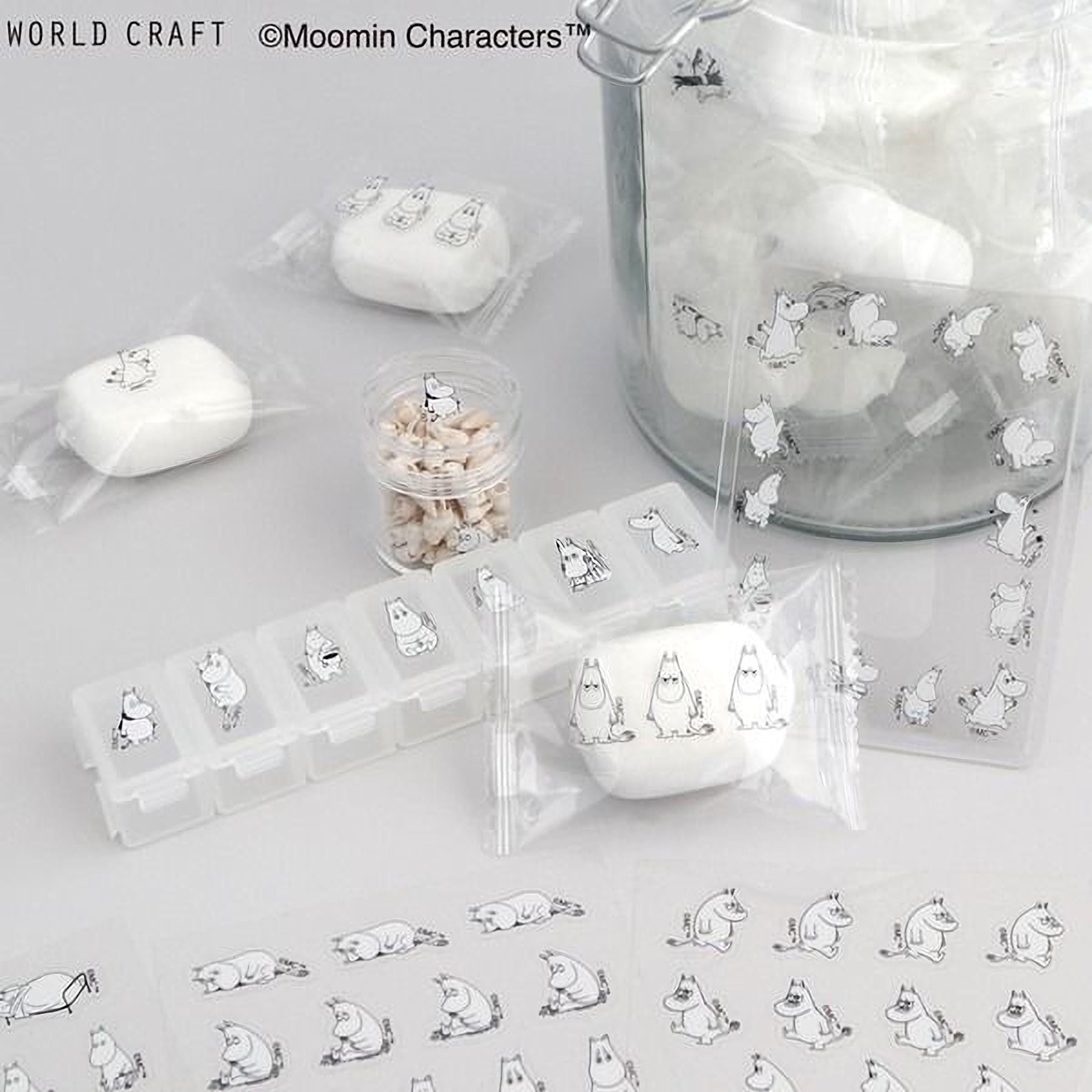 various items related to the Moomin character, including a glass jar filled with white objects, a pill organizer, and several small white objects. The items are arranged on a white surface, with some of them wrapped in clear plastic.