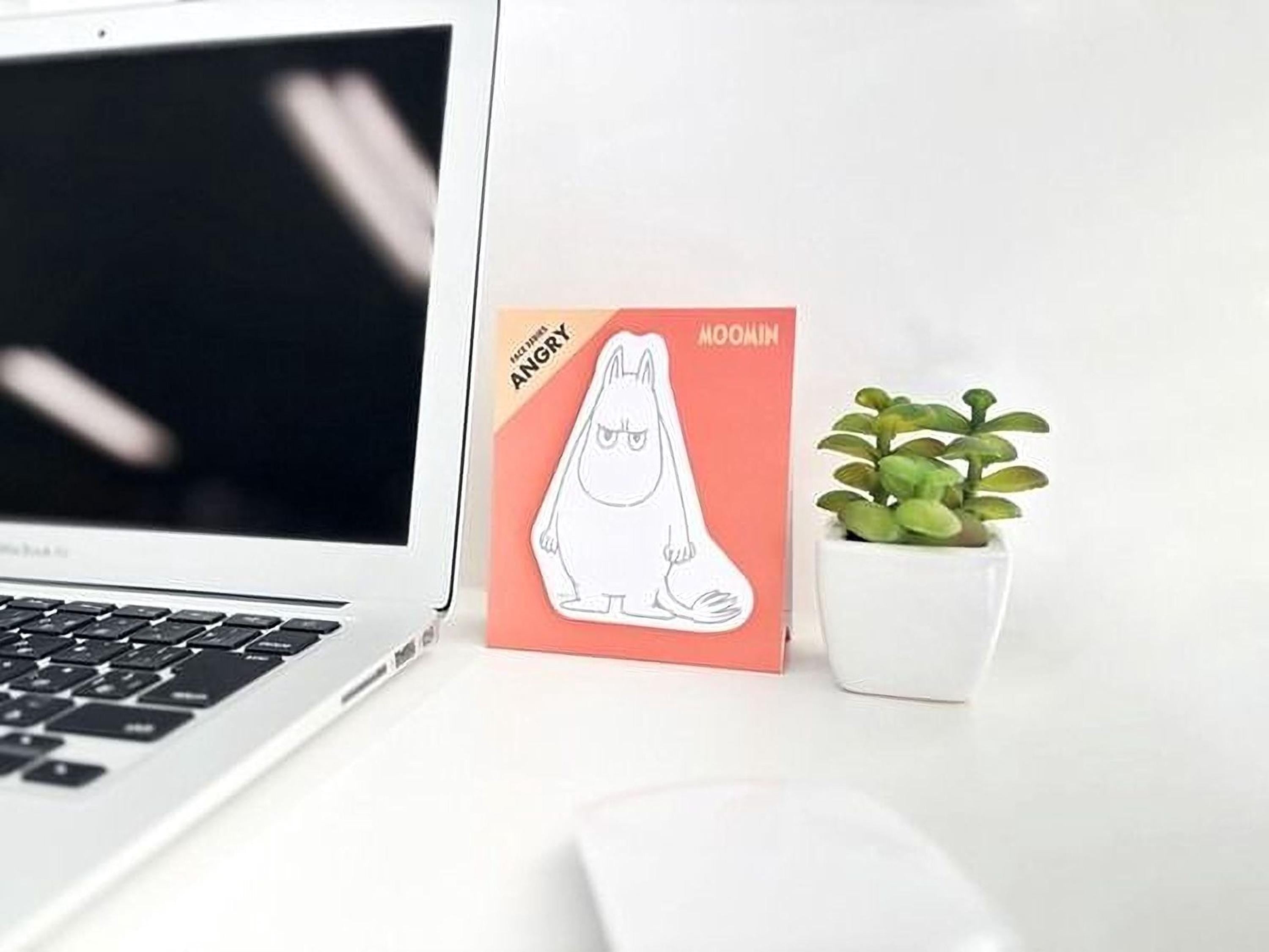 a laptop, a mouse, a potted plant, and a card with a cartoon character on a white desk.