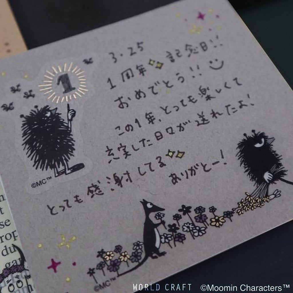 a handwritten note with various characters and illustrations, including a character holding a flower and a bird. The note appears to be in a foreign language, possibly Japanese, and is written on a piece of paper or card.