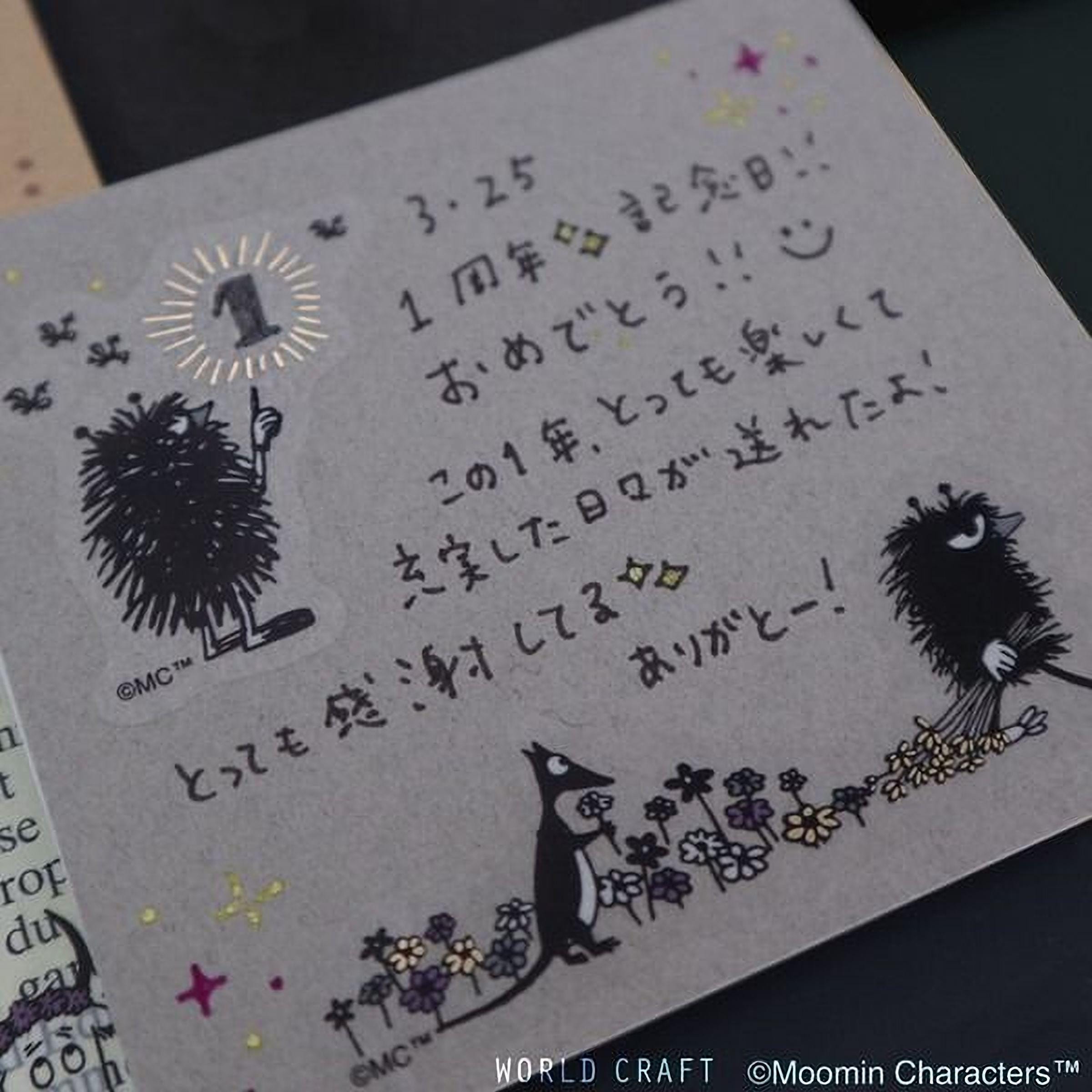 a handwritten note with various characters and illustrations, including a character holding a flower and a bird. The note appears to be in a foreign language, possibly Japanese, and is written on a piece of paper or card.
