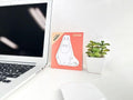 a laptop, a mouse, a potted plant, and a card with a cartoon character on a white desk.