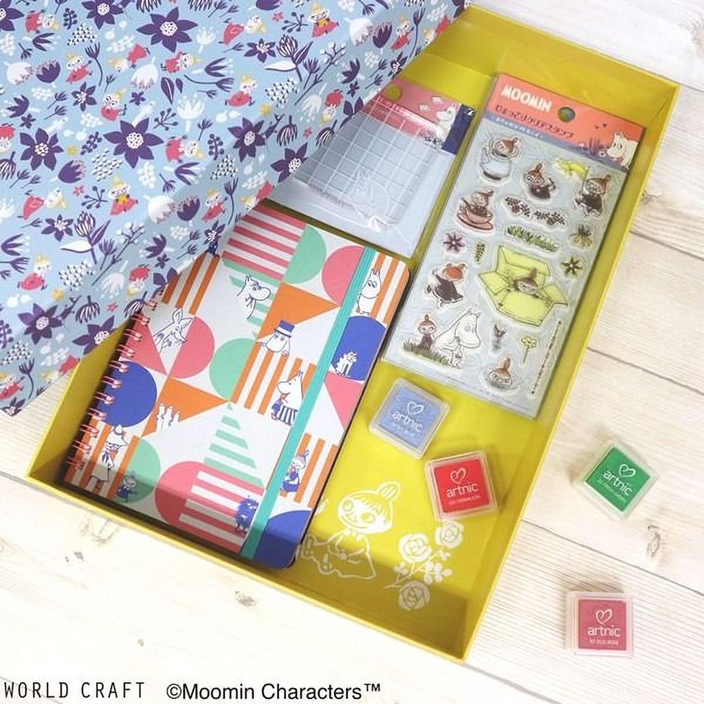 A yellow box containing various craft supplies, including a notebook, stickers, and markers, along with a blue and white patterned fabric.
