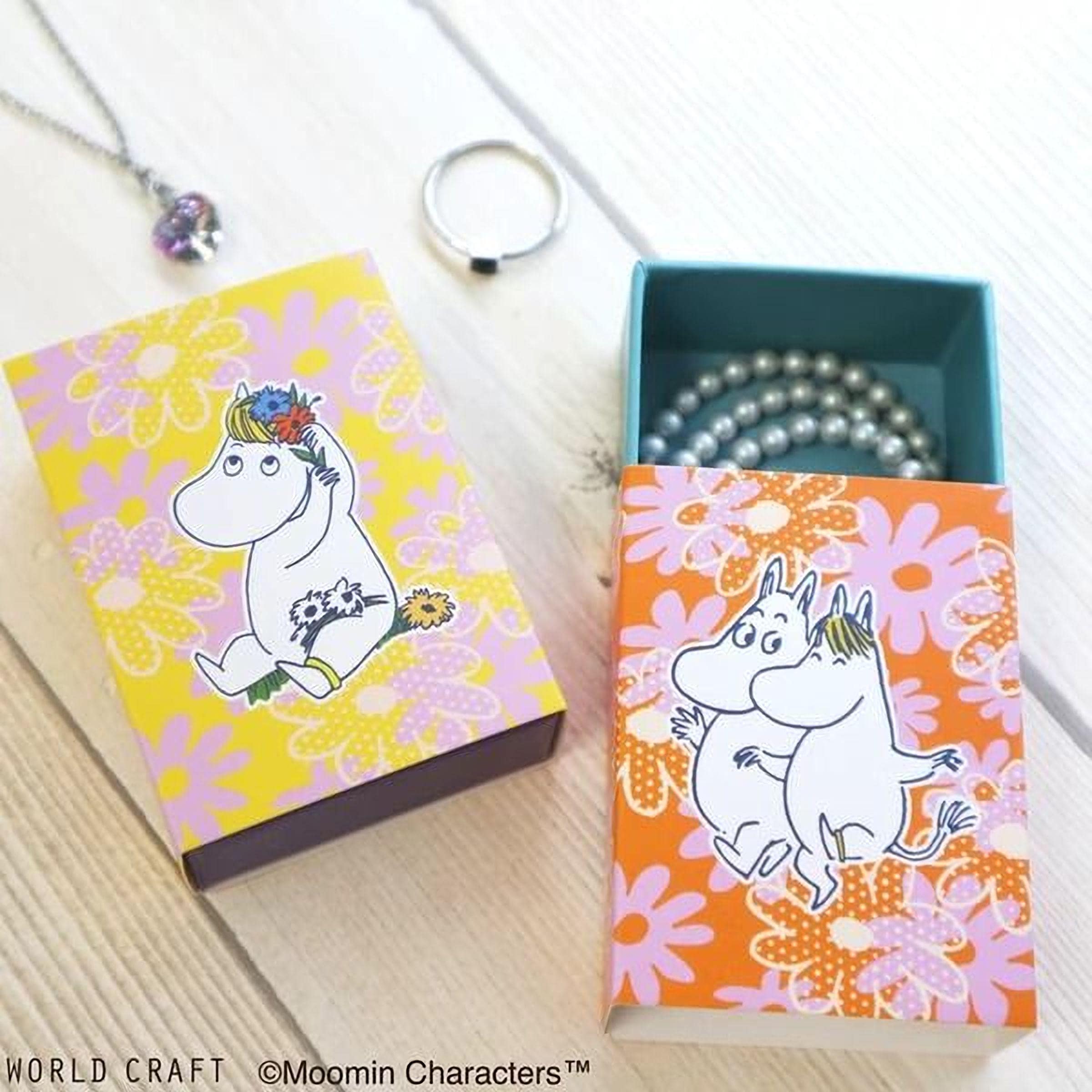 two boxes with illustrations of Moomin characters, one open to reveal pearls and the other closed. There is also a necklace and a ring visible in the scene.