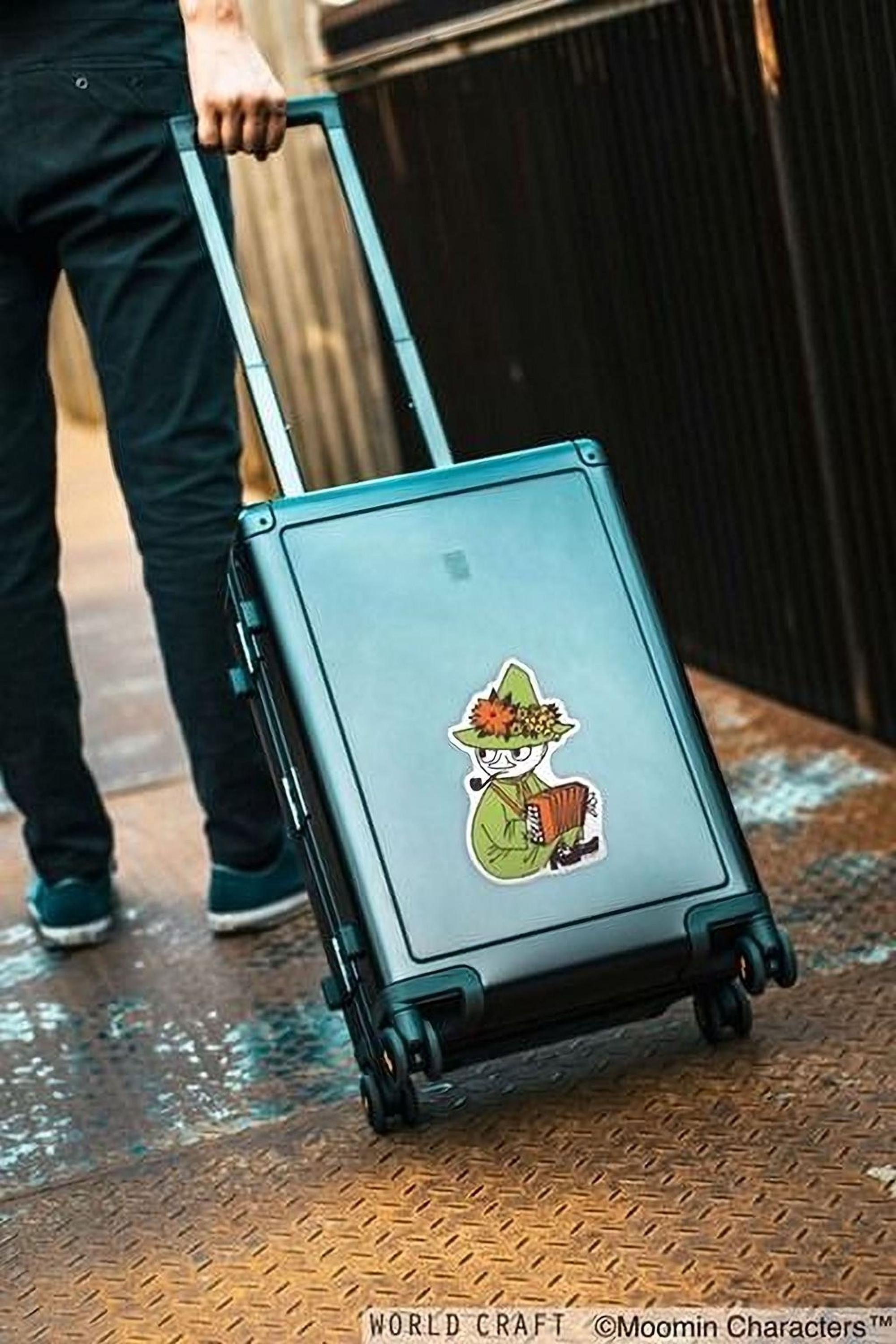 A person is pulling a suitcase with a sticker of a character on it, standing on a metal platform.