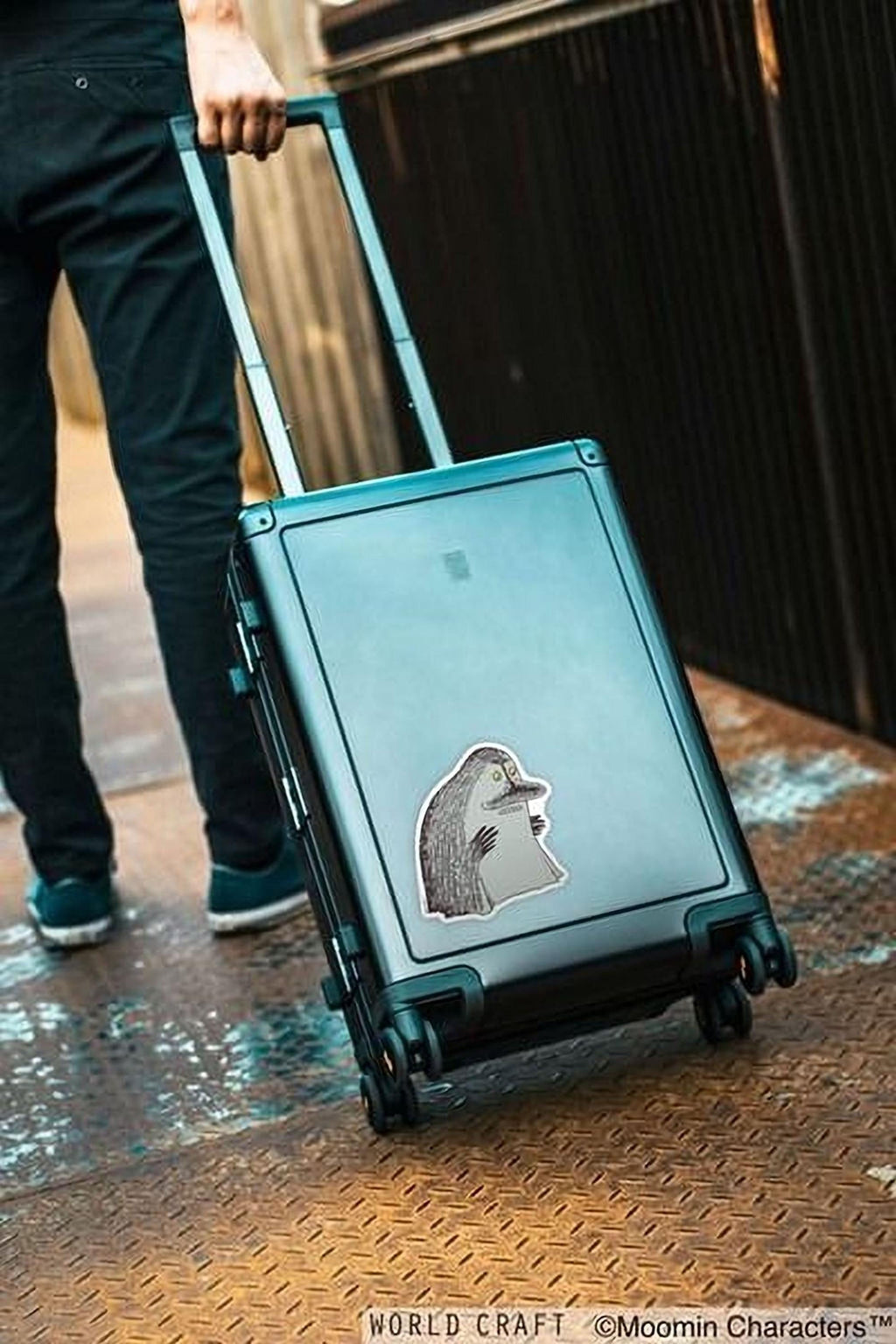 A person is pulling a suitcase with a sticker on it, standing on a metal platform.