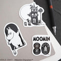 three stickers, each depicting a different Moomin character and a building. The stickers are arranged on a surface, with a pen and a piece of paper visible in the background.