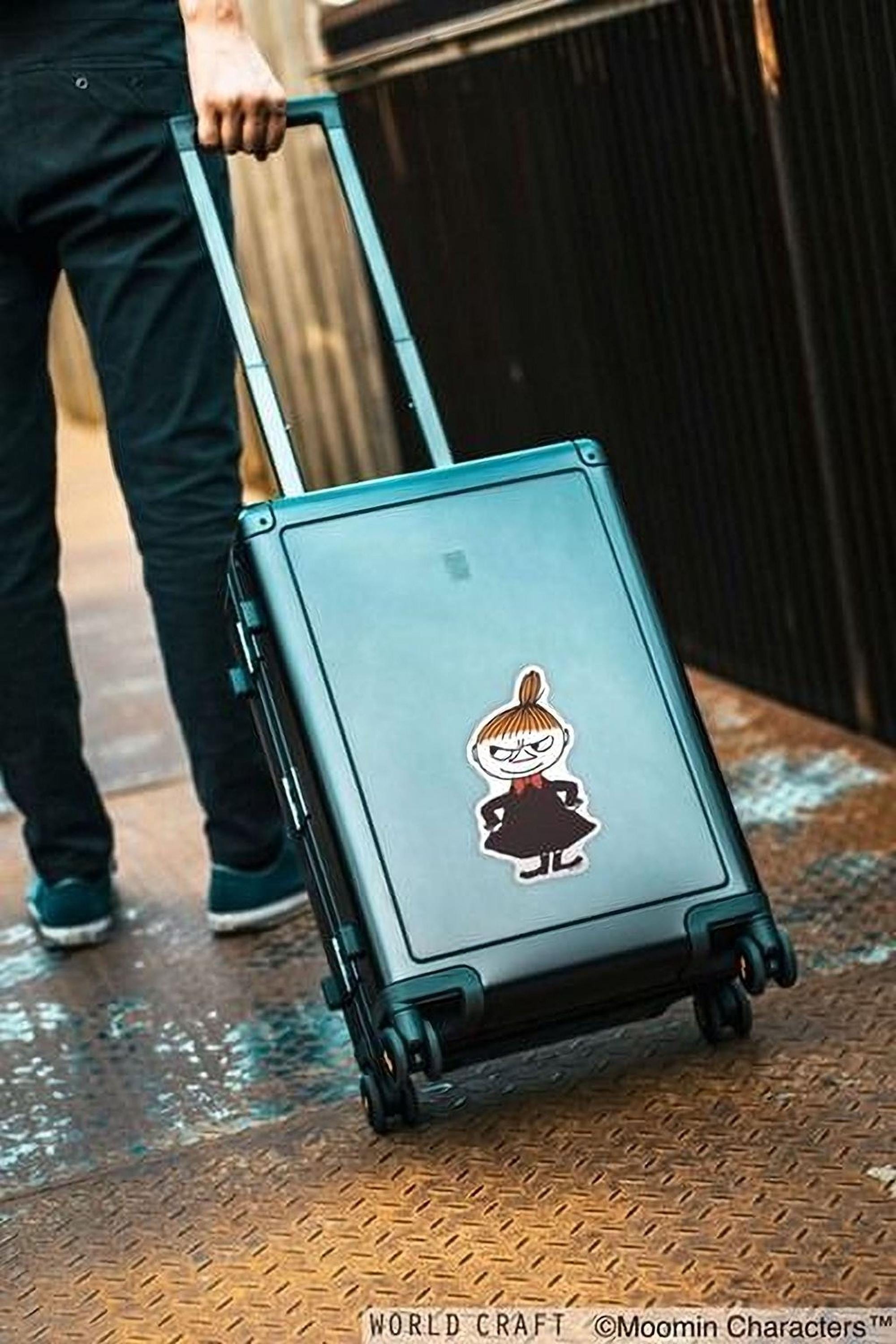 A person is pulling a suitcase with a cartoon character sticker on it, standing on a metal platform.