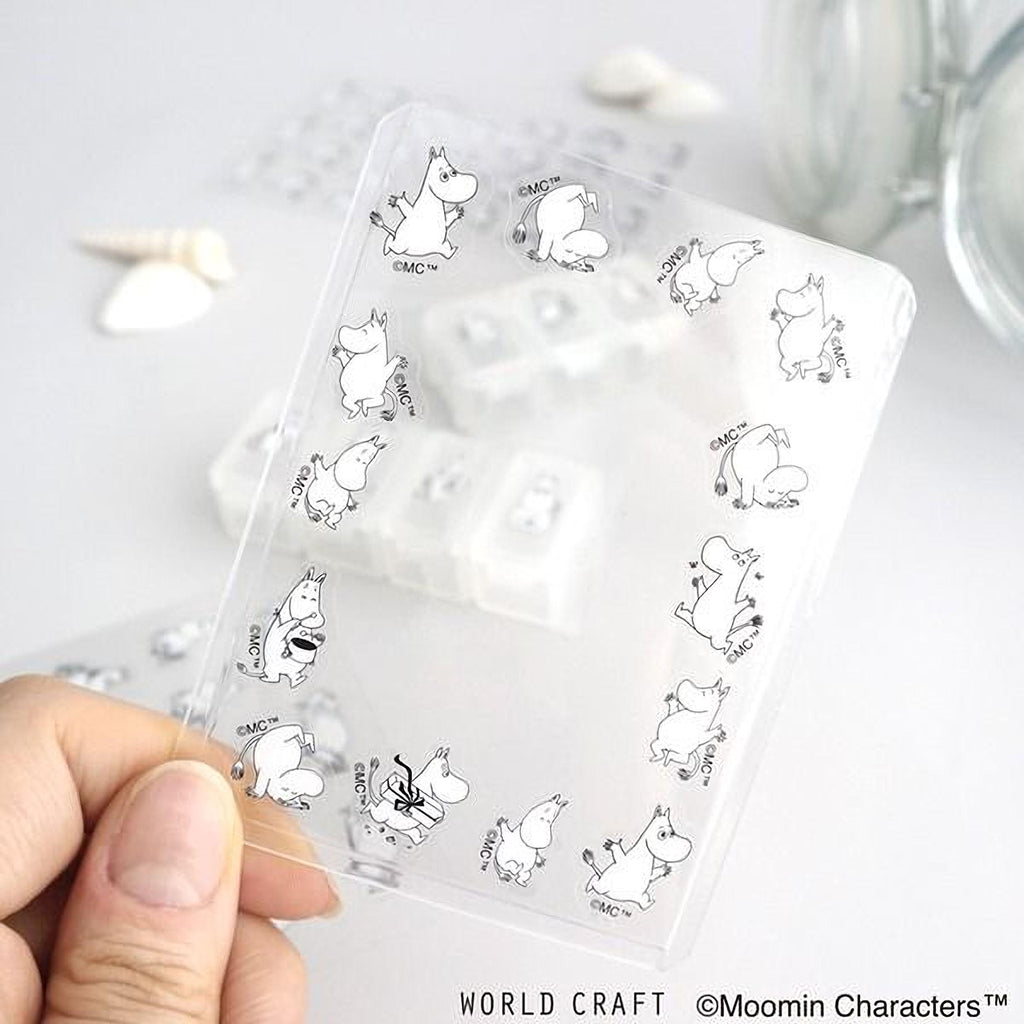 A hand is holding a clear card with a repeating pattern of Moomin characters, including various poses and expressions.
