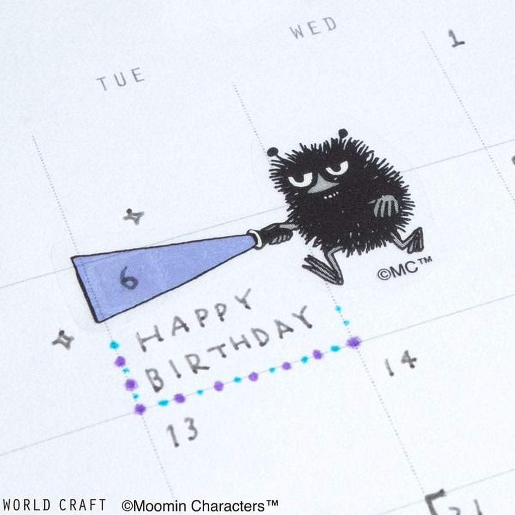 A calendar page with a playful illustration of a fuzzy black creature holding a blue megaphone and the text "Happy Birthday" written below it.