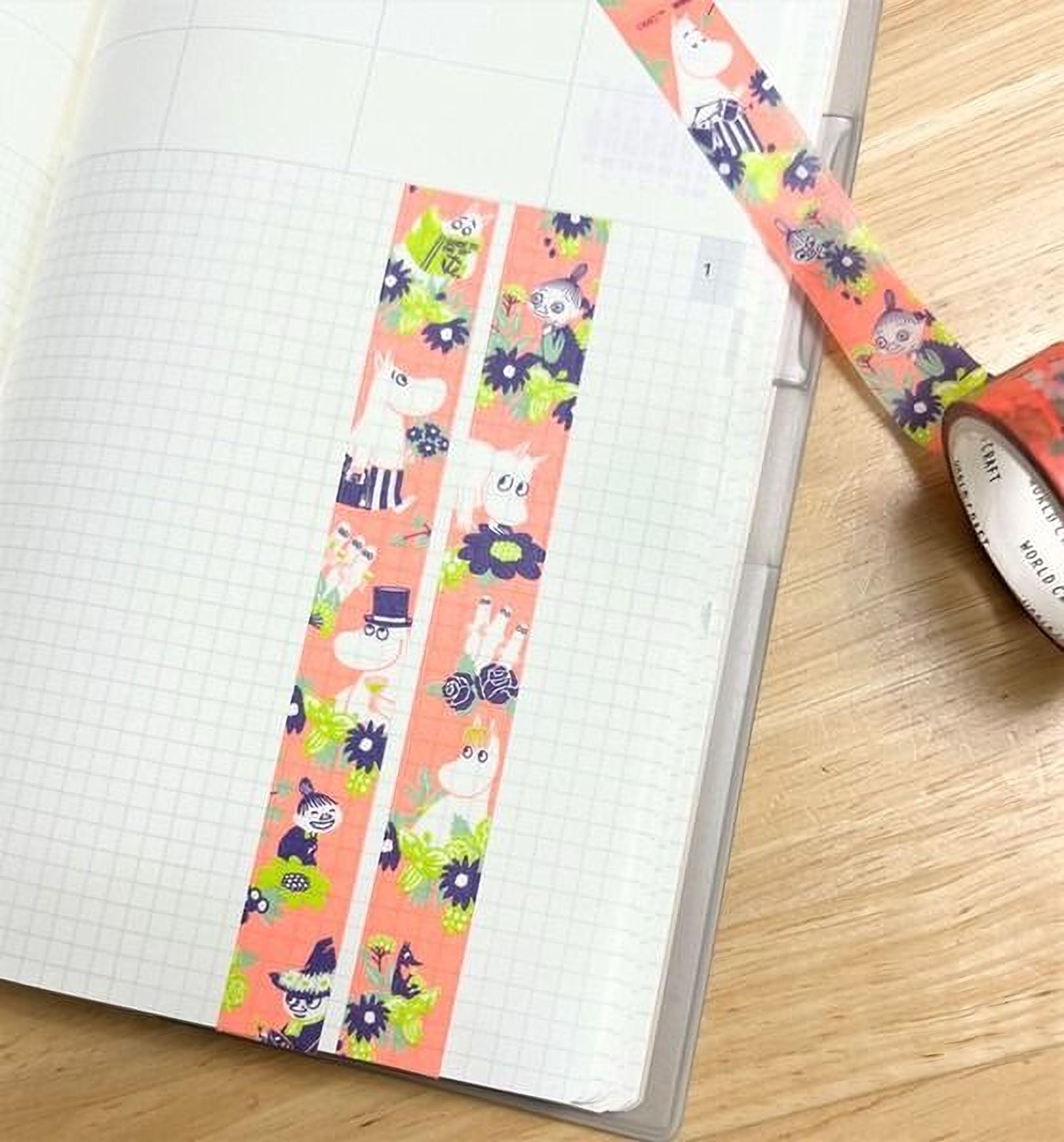 a notebook with a grid pattern, and there is a roll of tape with a colorful, cartoonish design on it.