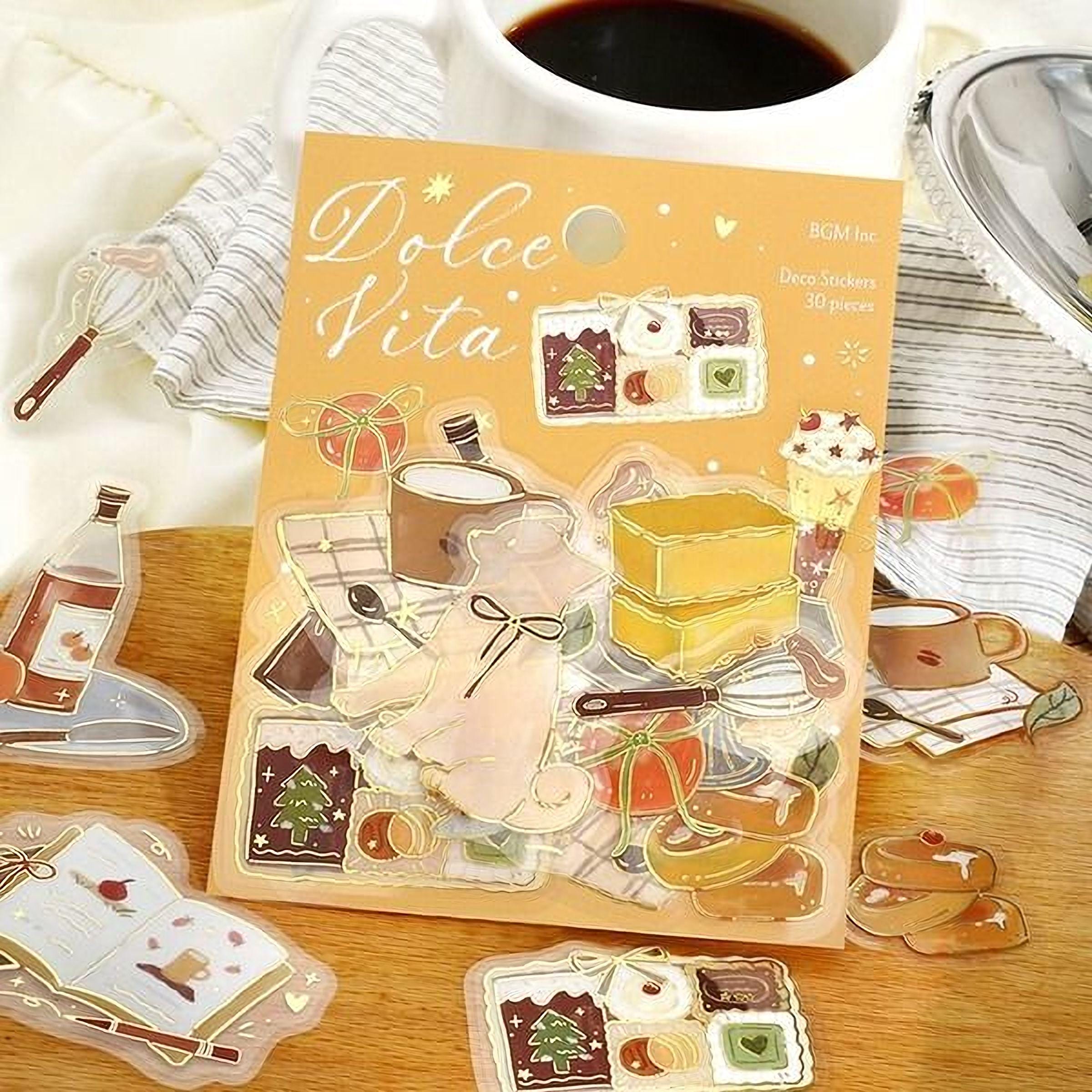 a package of stickers with various food-related items, such as a cup, spoon, cake, and other kitchen utensils, as well as a coffee cup and a teapot. The stickers are arranged on a wooden surface, and there is a cup of coffee nearby.
