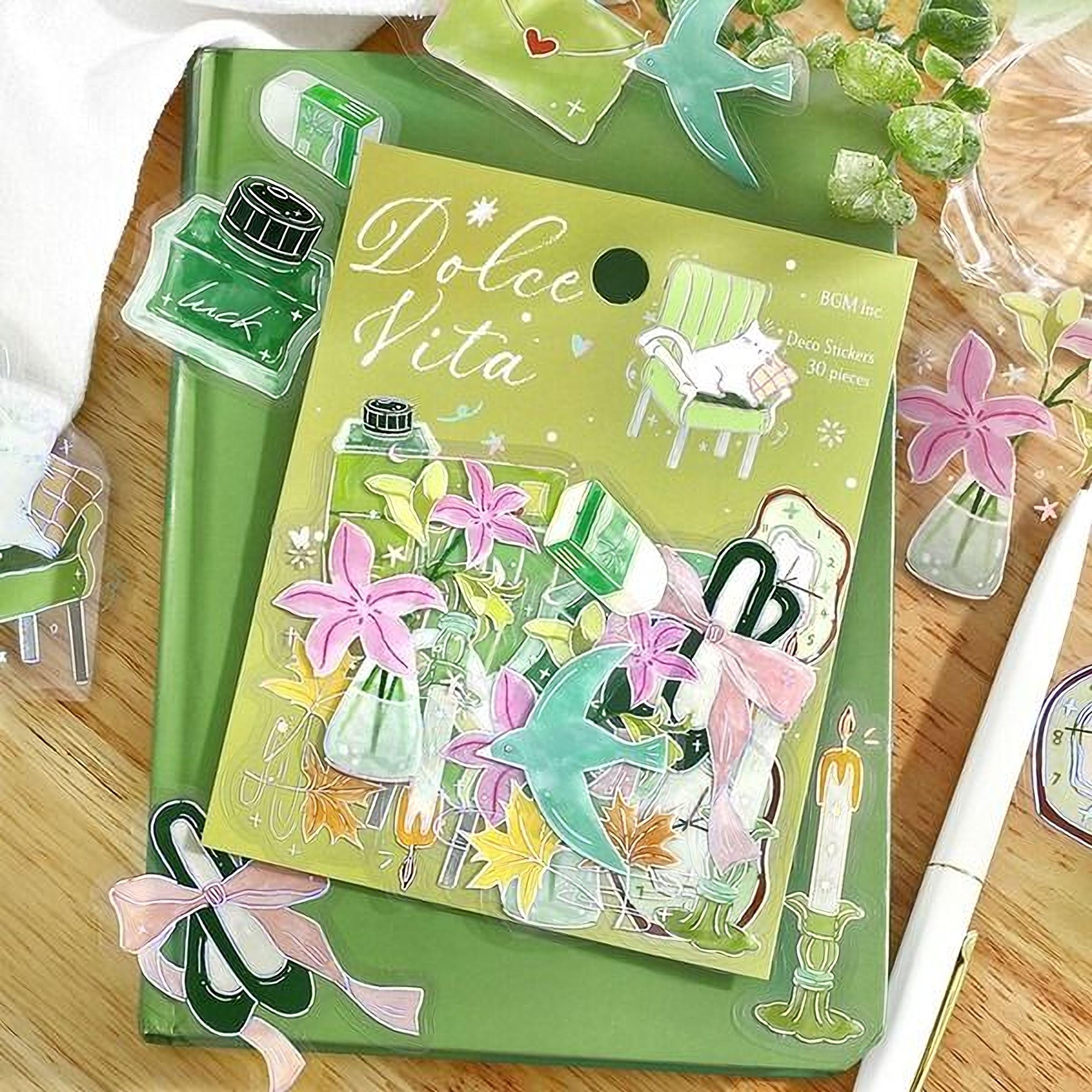 a green notebook with a variety of colorful stickers and illustrations on the cover, including flowers, plants, and other decorative elements.