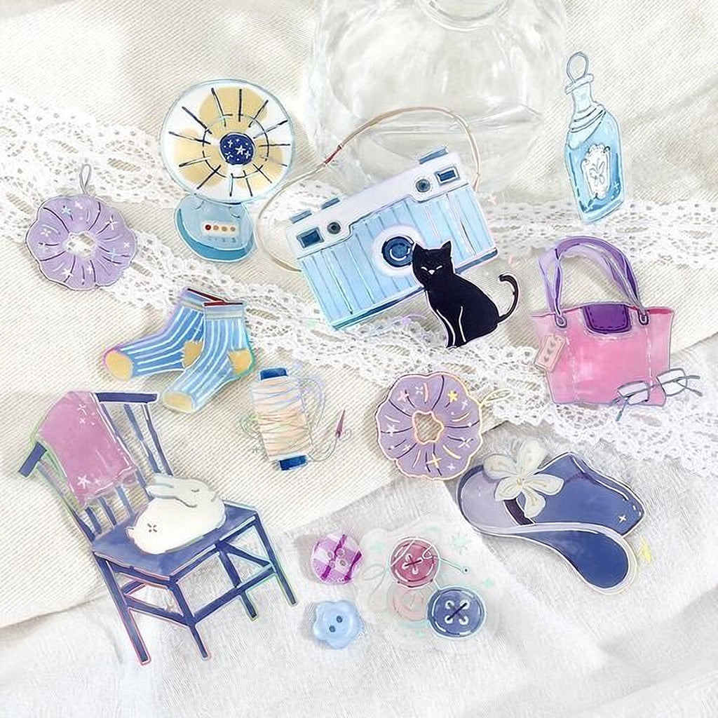 various colorful and whimsical objects, including a fan, camera, flowers, a cat, a pink purse, and a pair of shoes, all arranged on a white surface with lace trim.