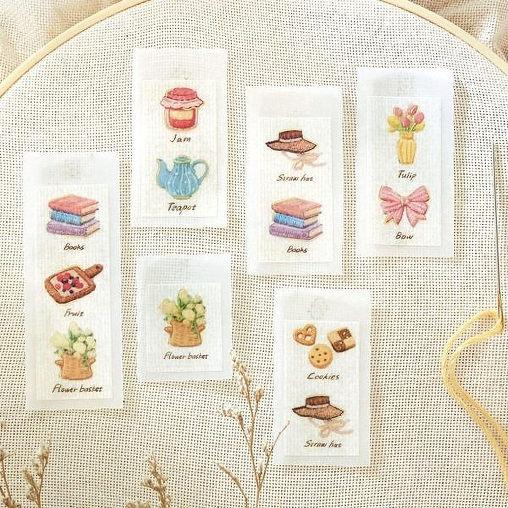 six embroidered labels with various illustrations, including books, fruits, flowers, cookies, and other items, all set against a beige background.