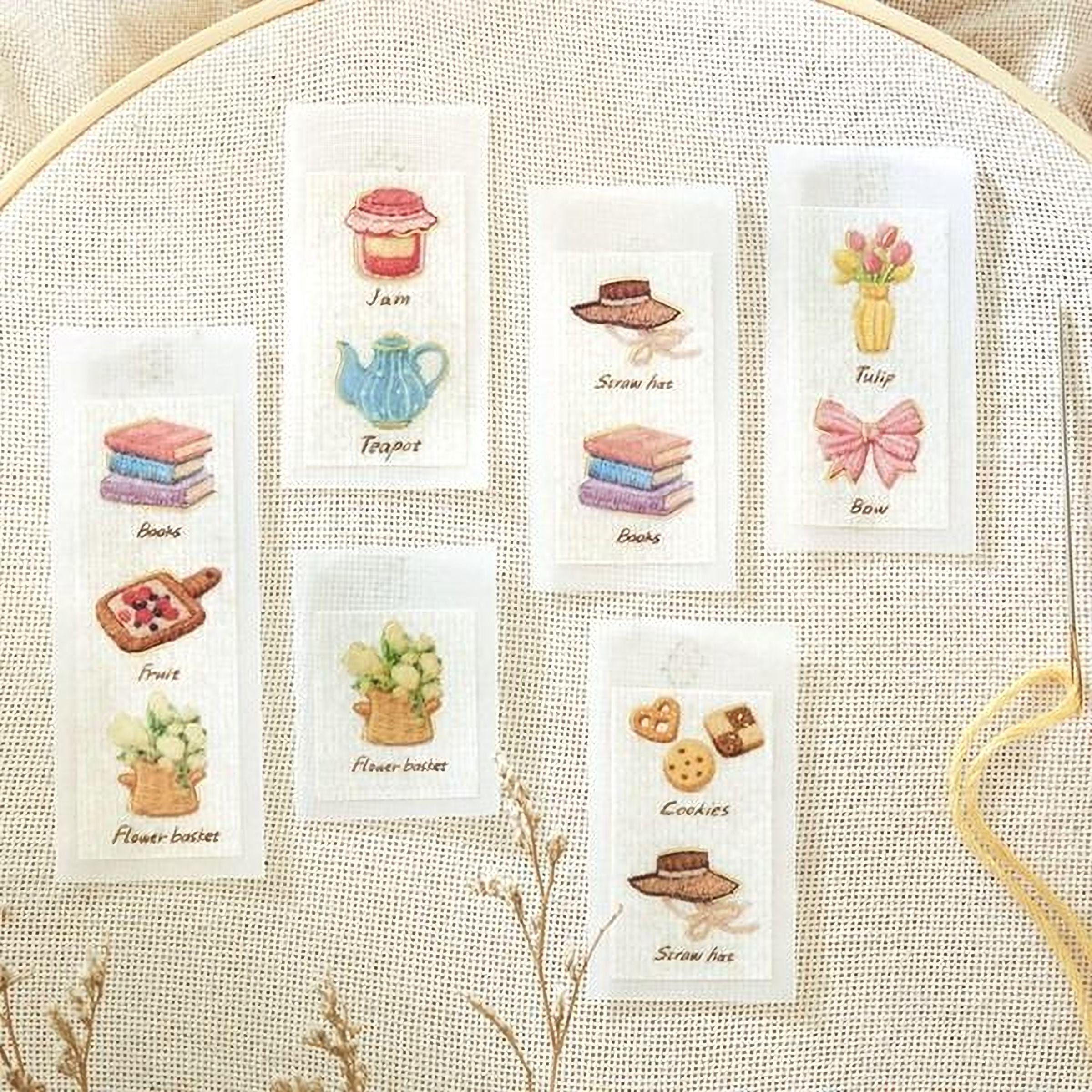 six embroidered labels with various illustrations, including books, fruits, flowers, cookies, and other items, all set against a beige background.