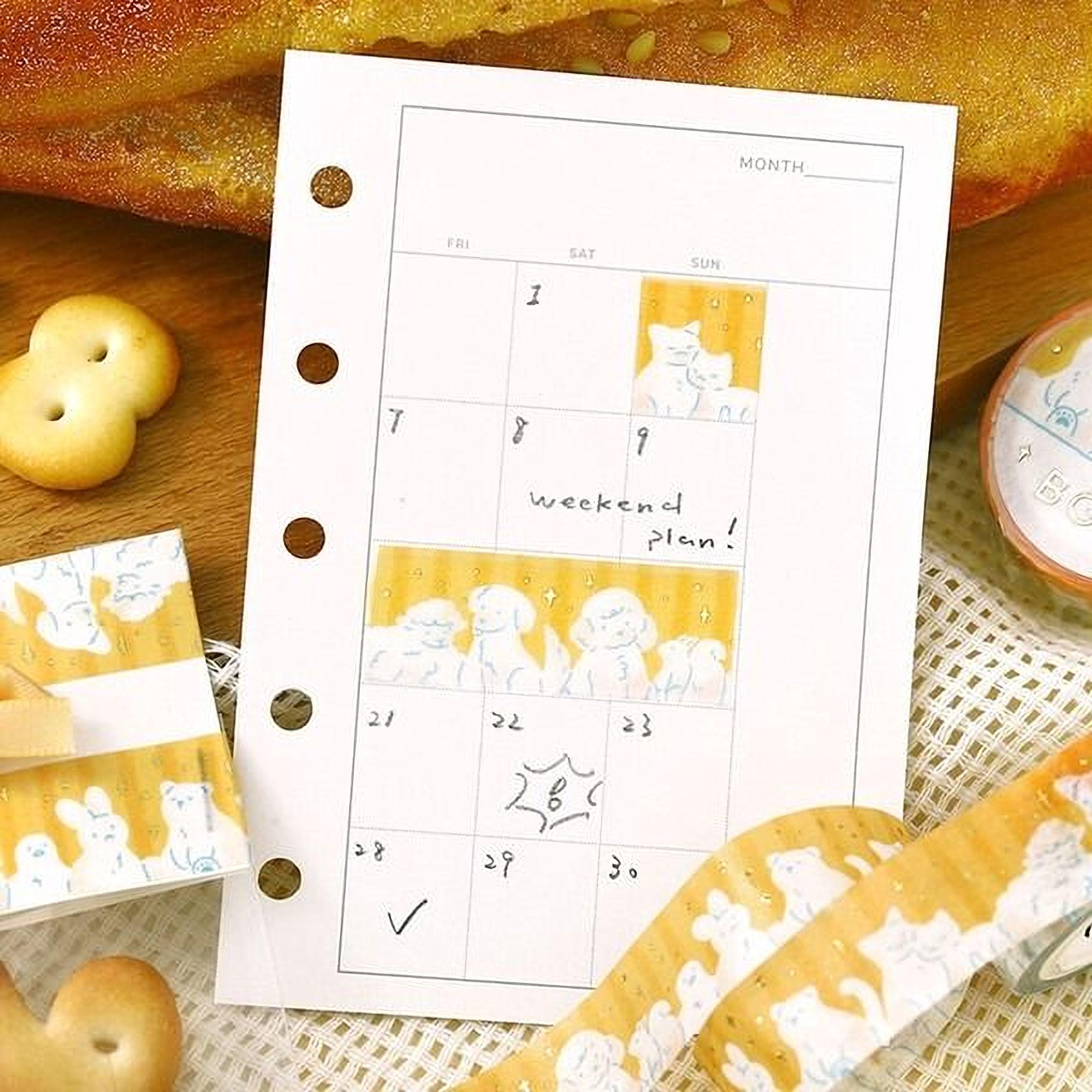 a calendar with a yellow and white color scheme, surrounded by various items such as cookies, a roll of tape, and a notebook.