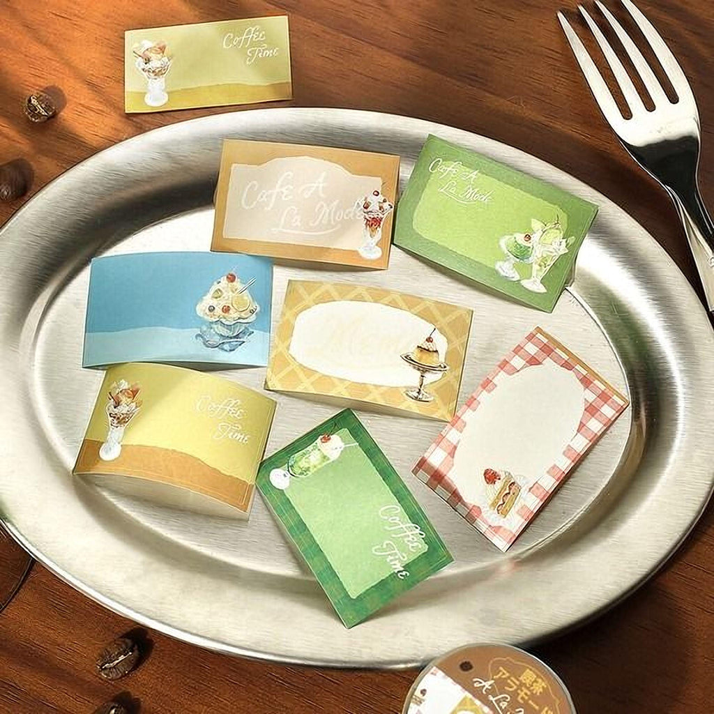 a silver plate with various colorful paper cards or labels, including one that says "Cafe a la Mode", and a fork is placed next to the plate.