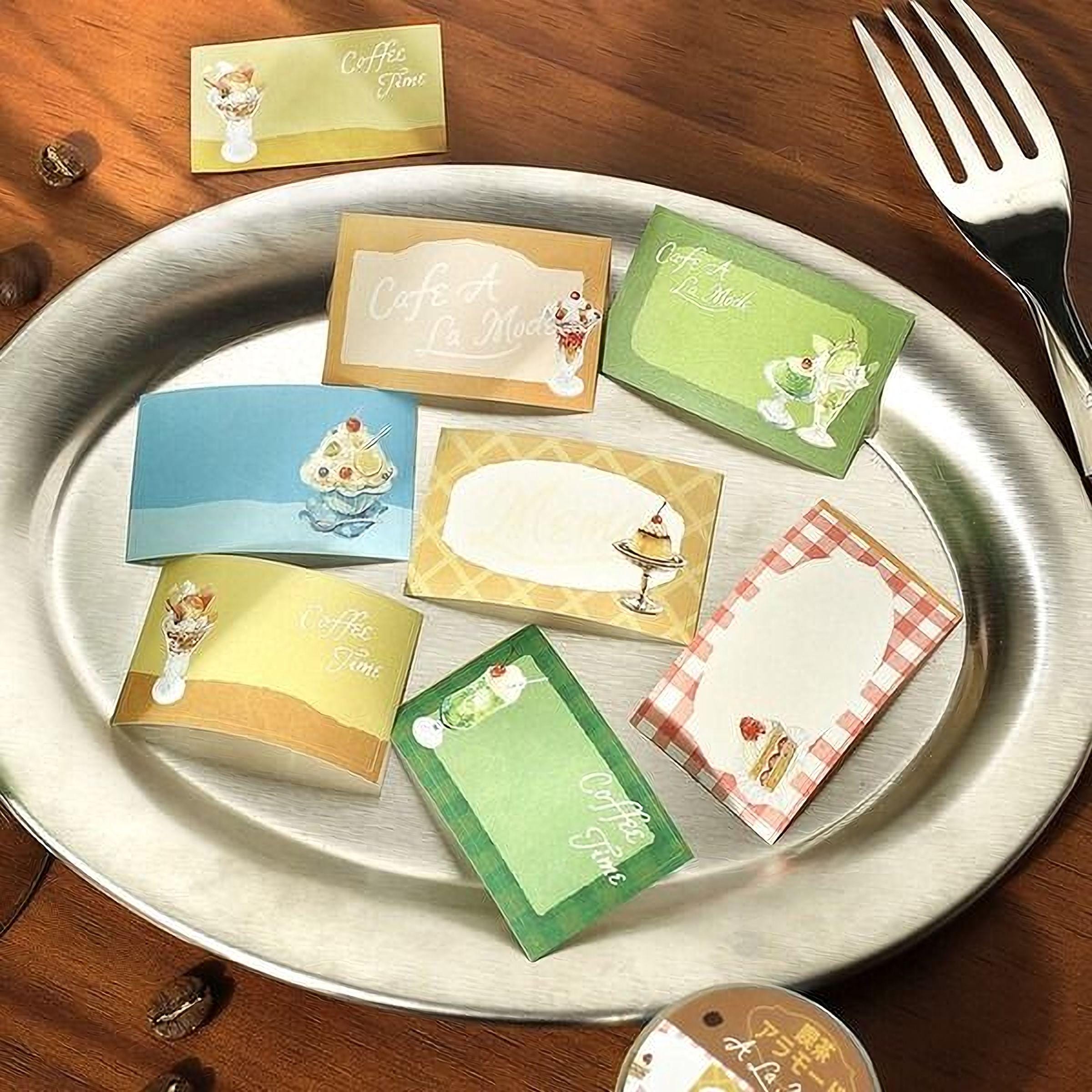a silver plate with various colorful paper cards or labels, including one that says "Cafe a la Mode", and a fork is placed next to the plate.