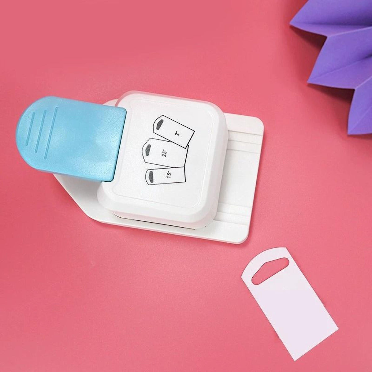 a white hole puncher with a blue handle, placed on a pink background. There is also a white paper tag with a hole in it, positioned next to the hole puncher.