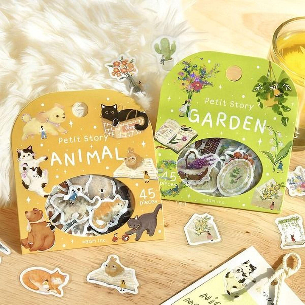 two packages of stickers, one yellow and one green, both labeled as "Petit Story" and "Animal" respectively. The packages are placed on a wooden surface, surrounded by various stickers and a glass of what appears to be juice.