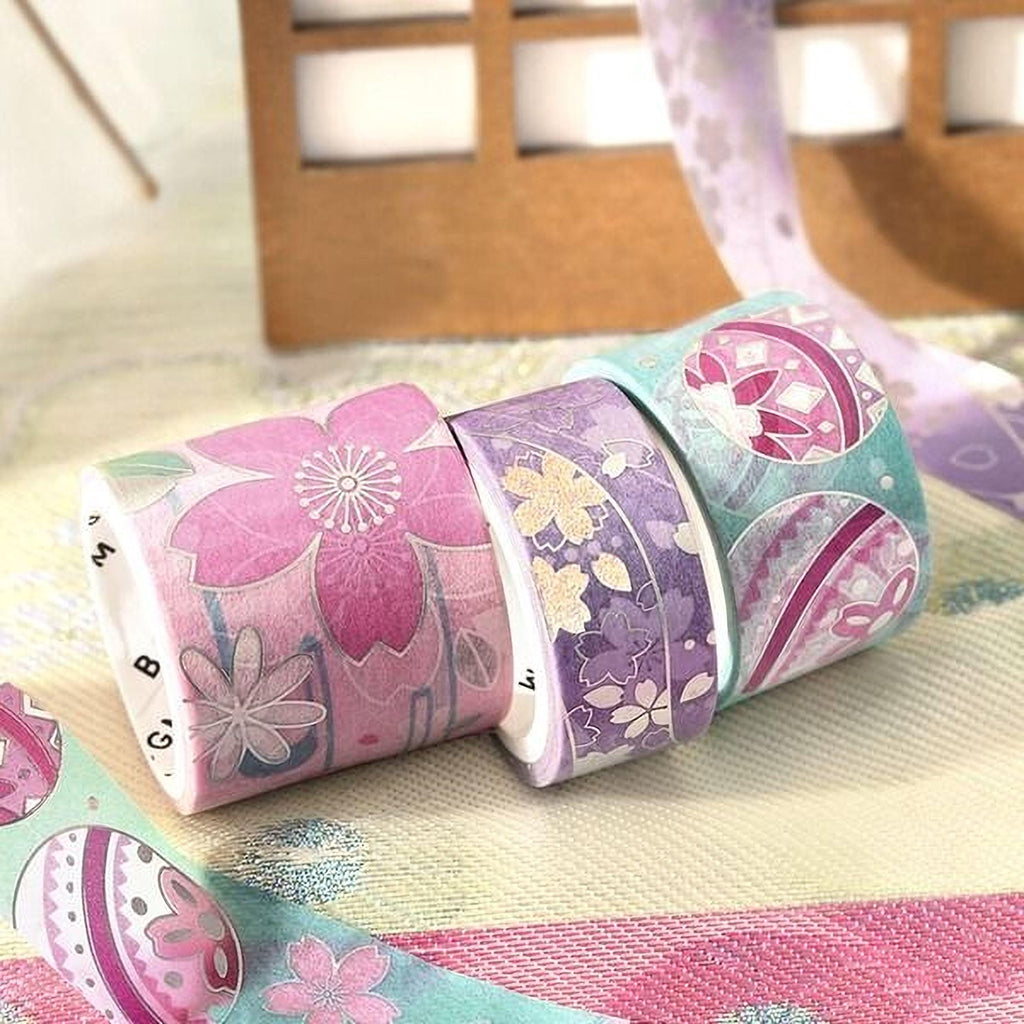 A collection of colorful patterned washi tape rolls arranged on a textured surface, with a wooden box visible in the background.