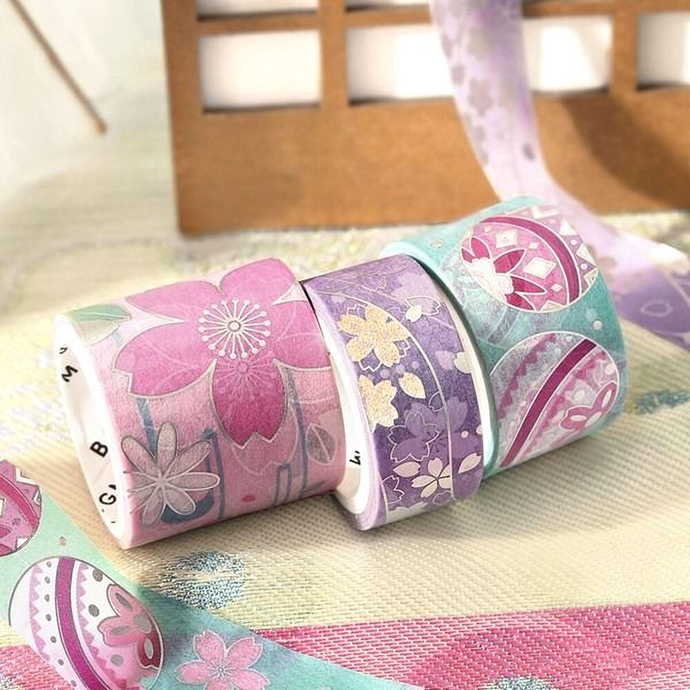 A collection of colorful patterned washi tape rolls arranged on a textured surface, with a wooden box visible in the background.