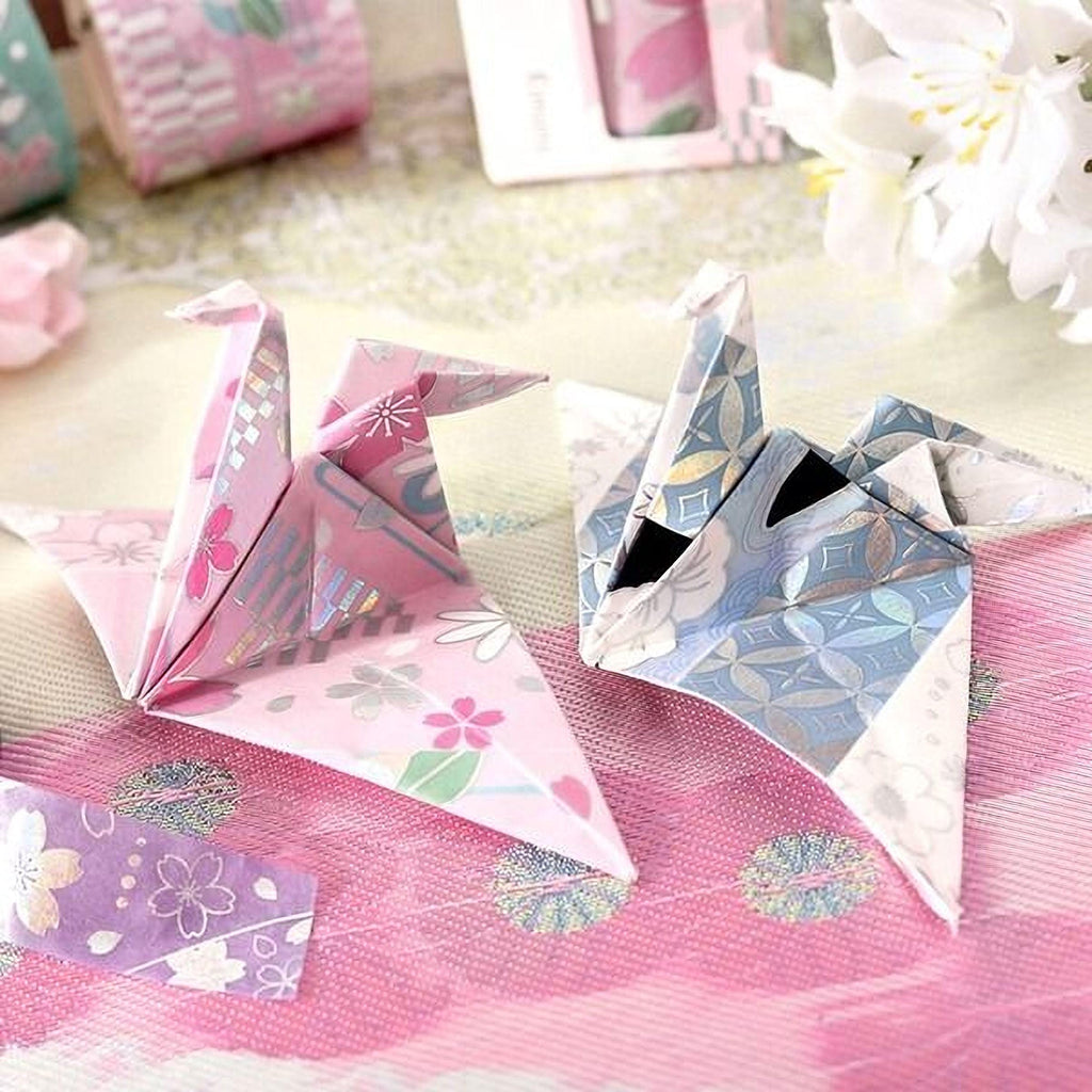 two origami birds, one pink and one blue, sitting on a pink and white floral background.