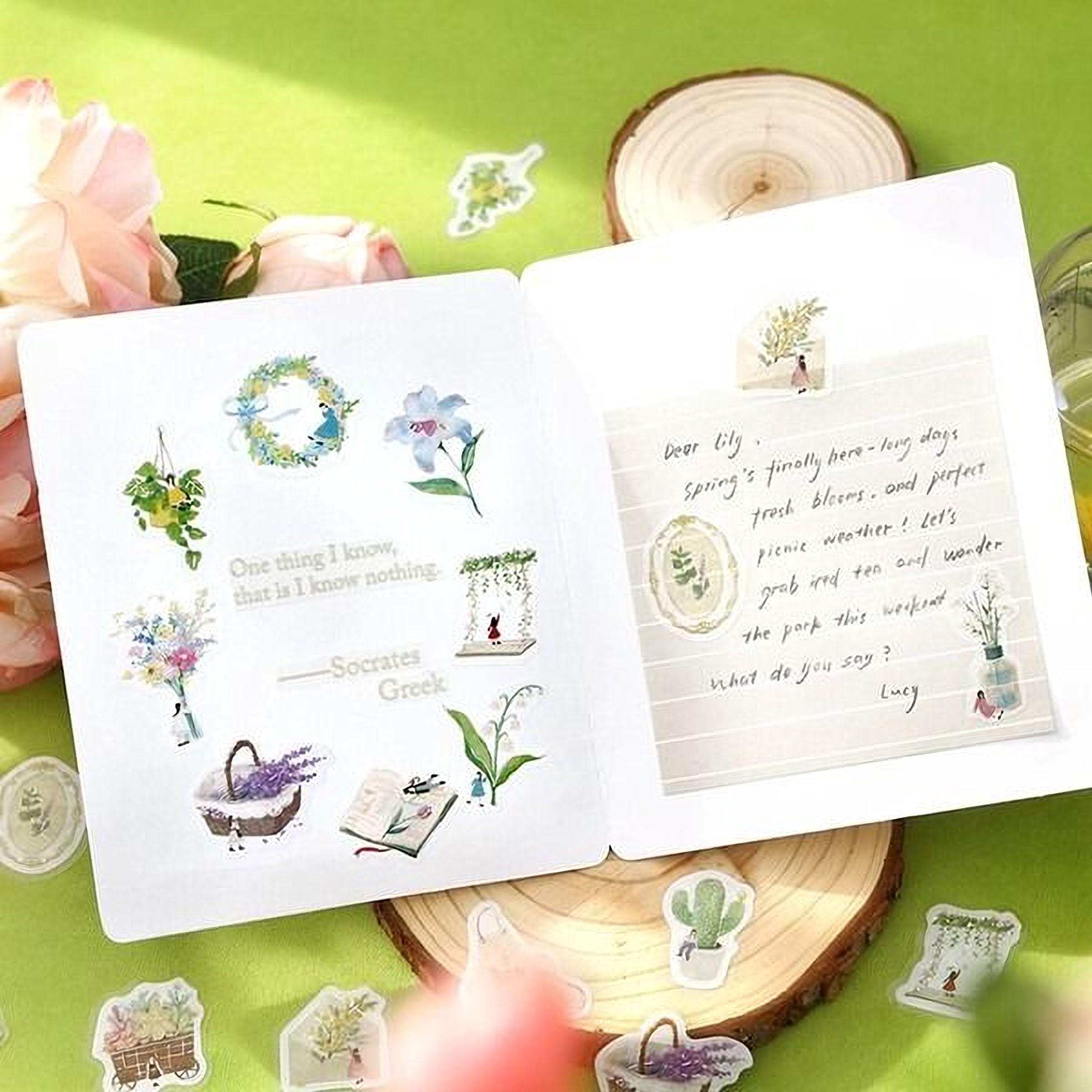 a white card with various stickers and illustrations, including flowers, plants, and a handwritten note, placed on a green surface.