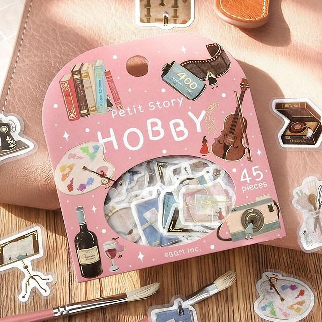 a pink box of stickers with various artistic and hobby-related stickers on it, along with a paintbrush and other art supplies.