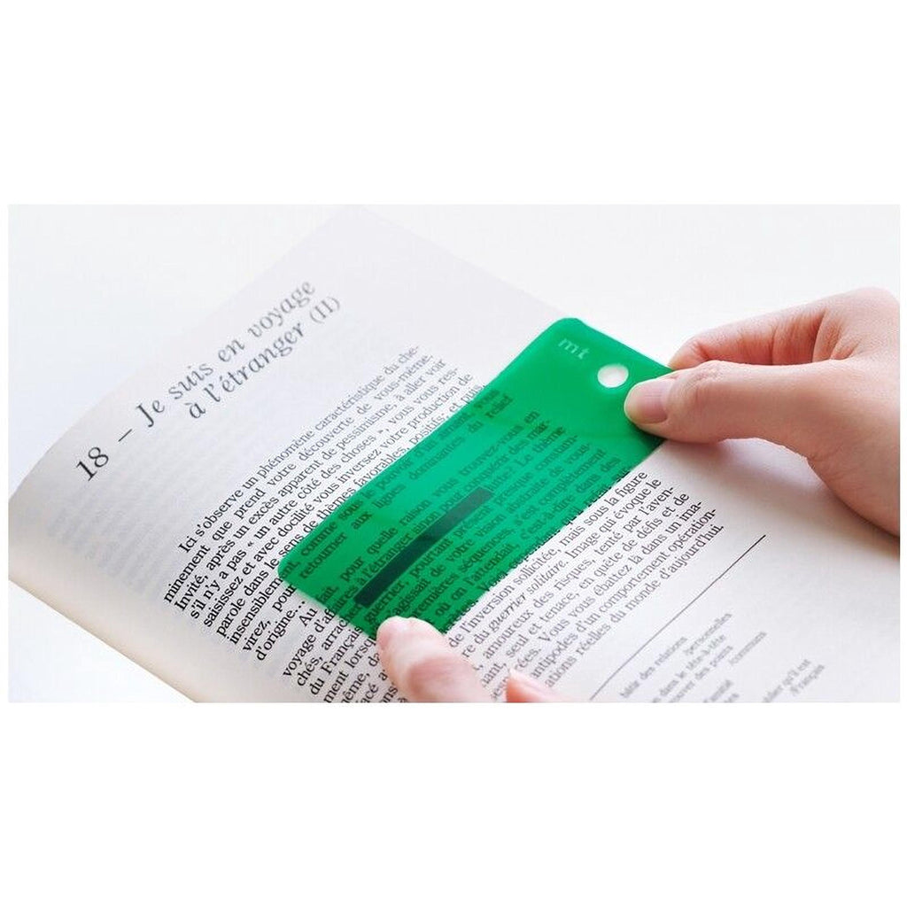 A person's hands are holding a green magnifying glass over a page of text in a book, which appears to be in French.