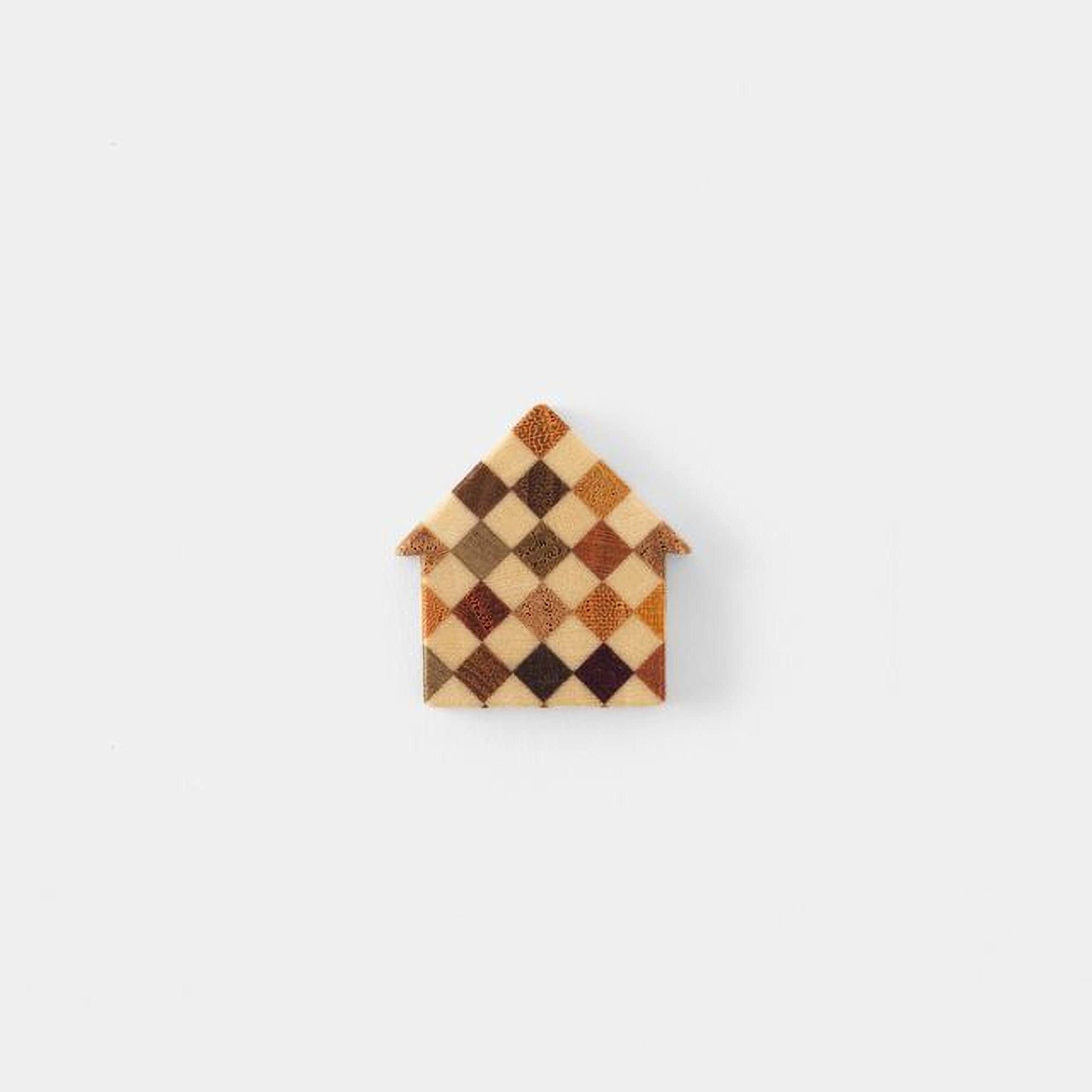 A small, colorful house-shaped object made of small squares or rectangles in various shades of brown, orange, and beige.