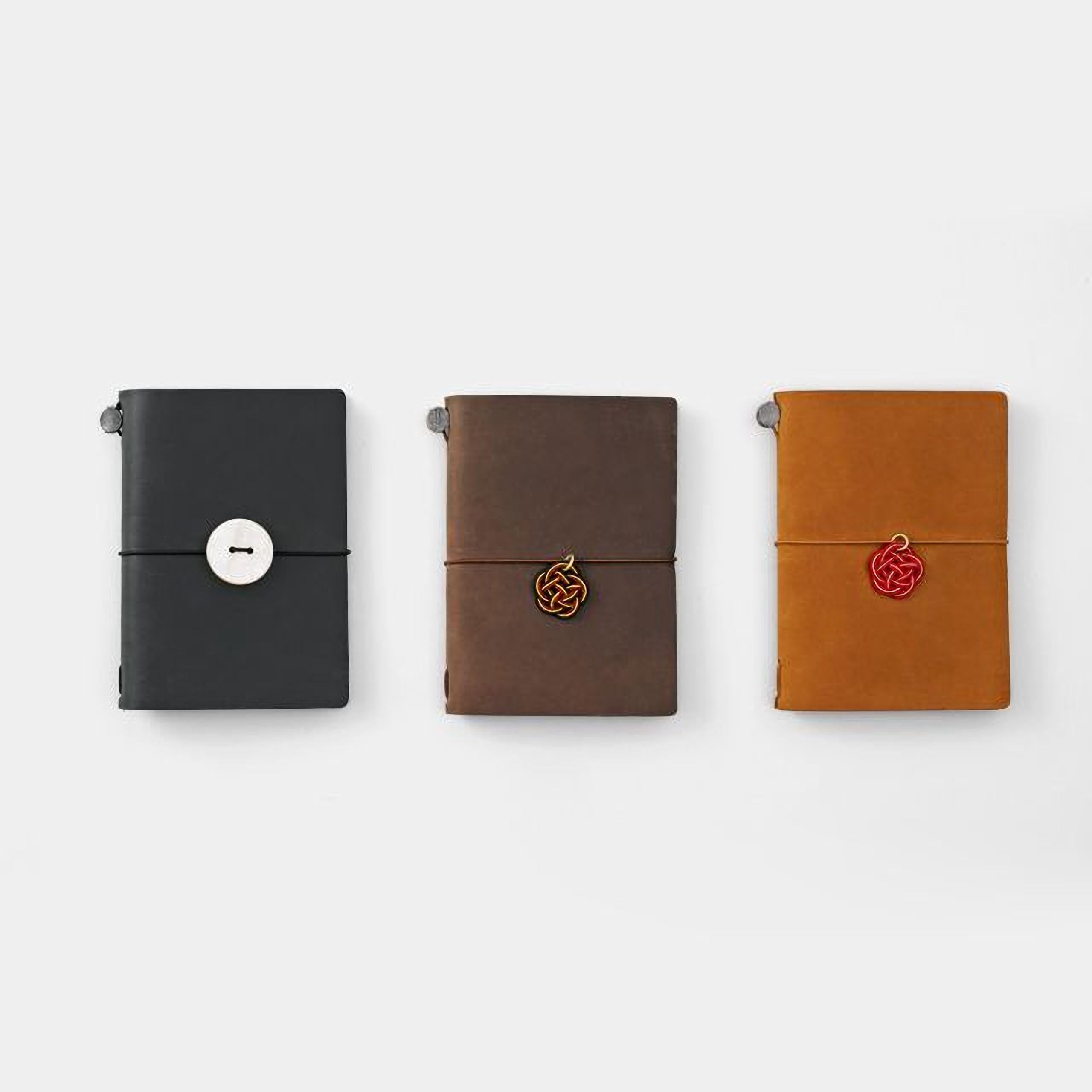 Three leather-bound notebooks in different colors - black, brown, and orange - are arranged in a row on a white background.