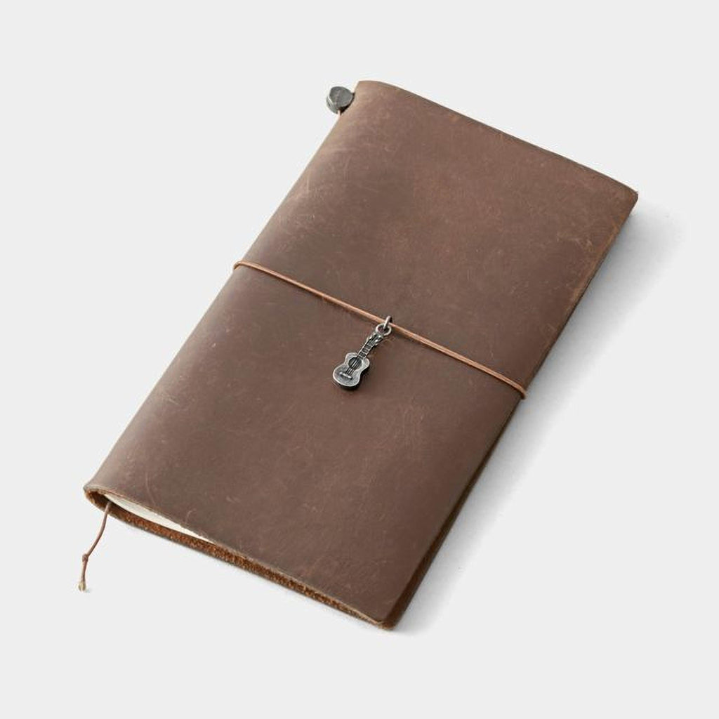 A brown leather-bound notebook with a metal guitar charm attached to the top.