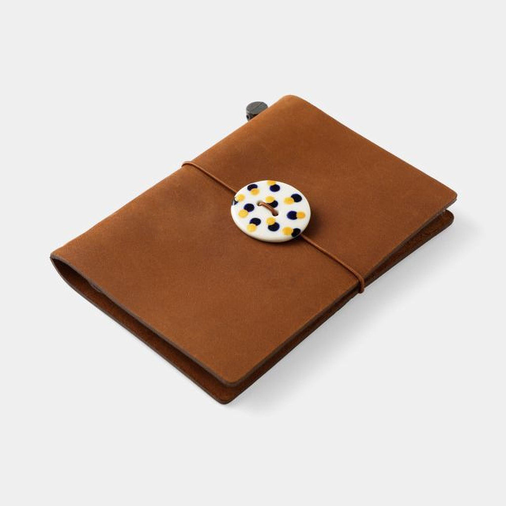 A brown leather-like notebook with a white and yellow polka dot button fastened with a string.
