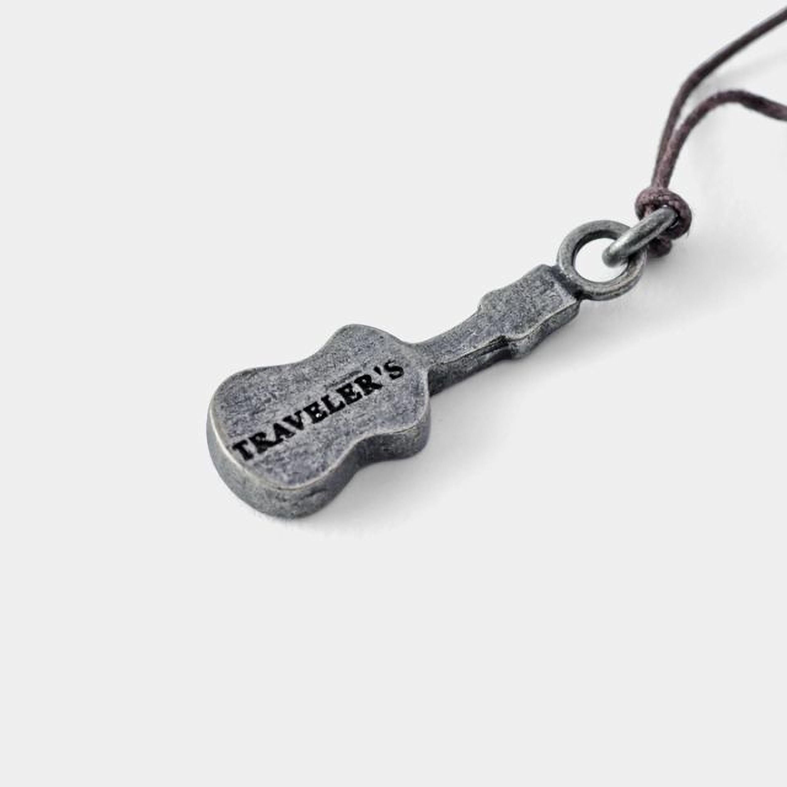 A silver-colored pendant in the shape of a guitar with the word "TRAVELER" engraved on it.
