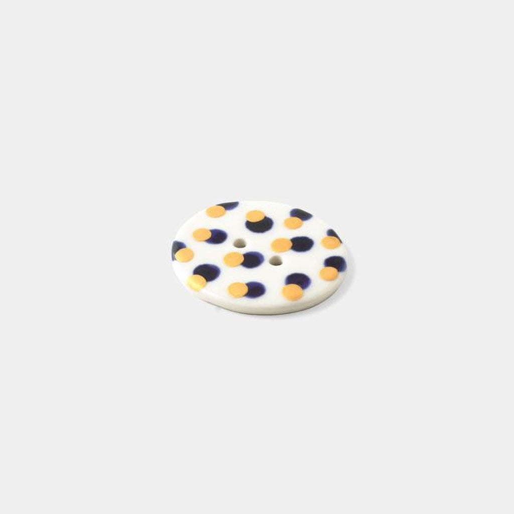 A white button with a pattern of yellow and blue dots is shown against a plain white background.