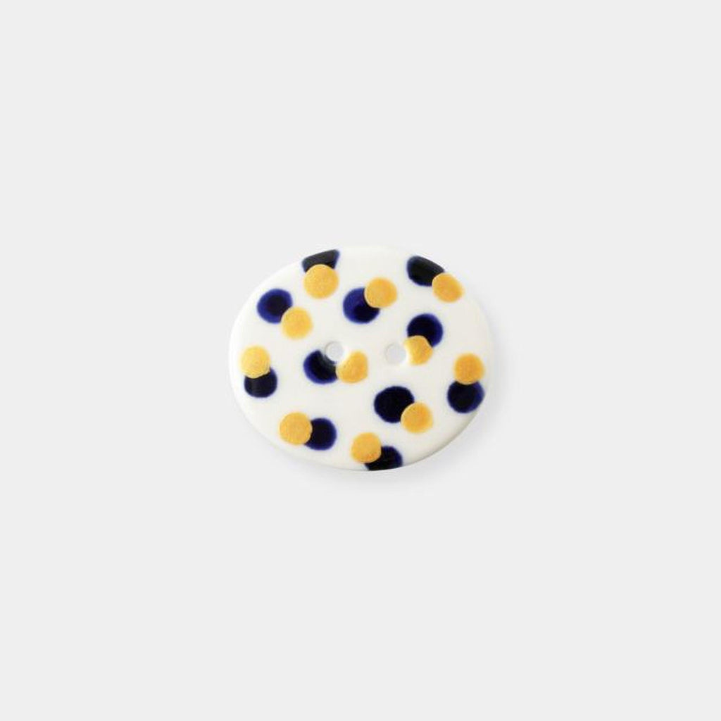 A white button with blue and yellow polka dots is shown against a plain white background.